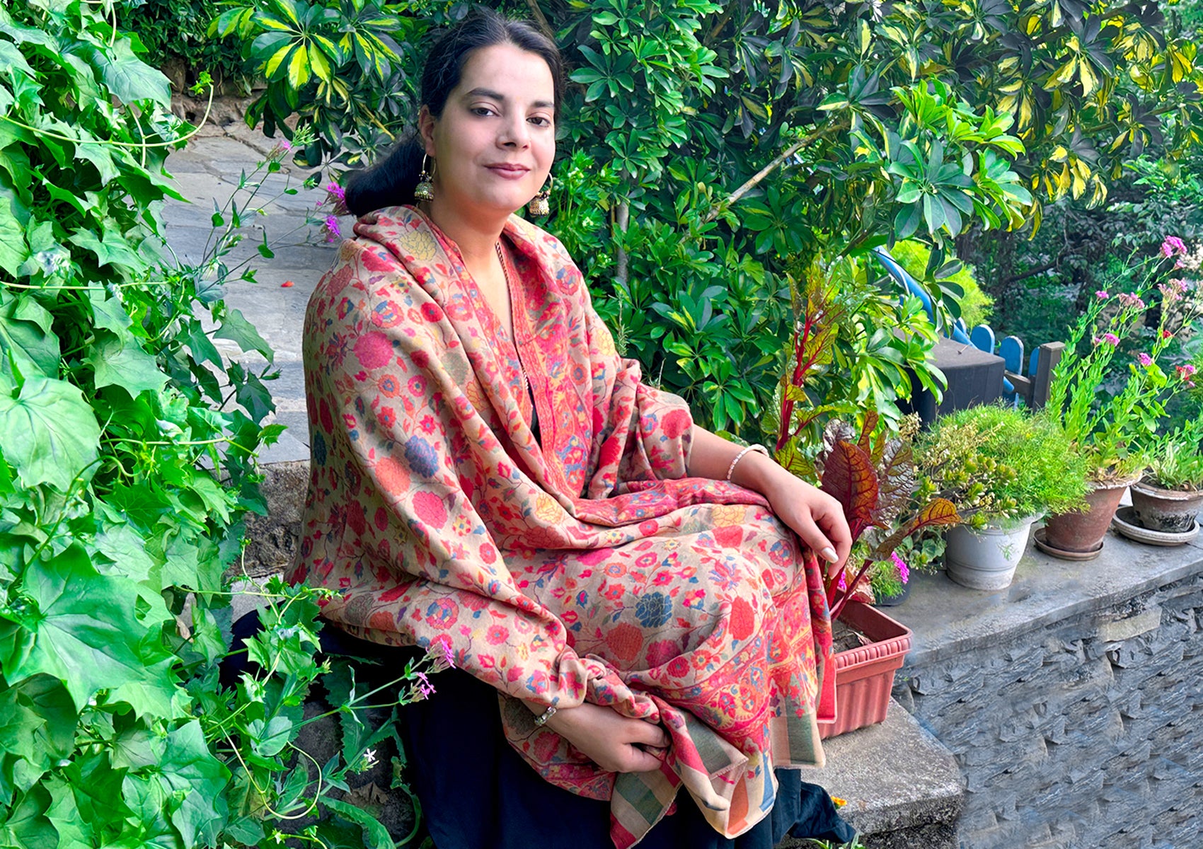 Woman wearing beige floral Kani shawl in a garden.