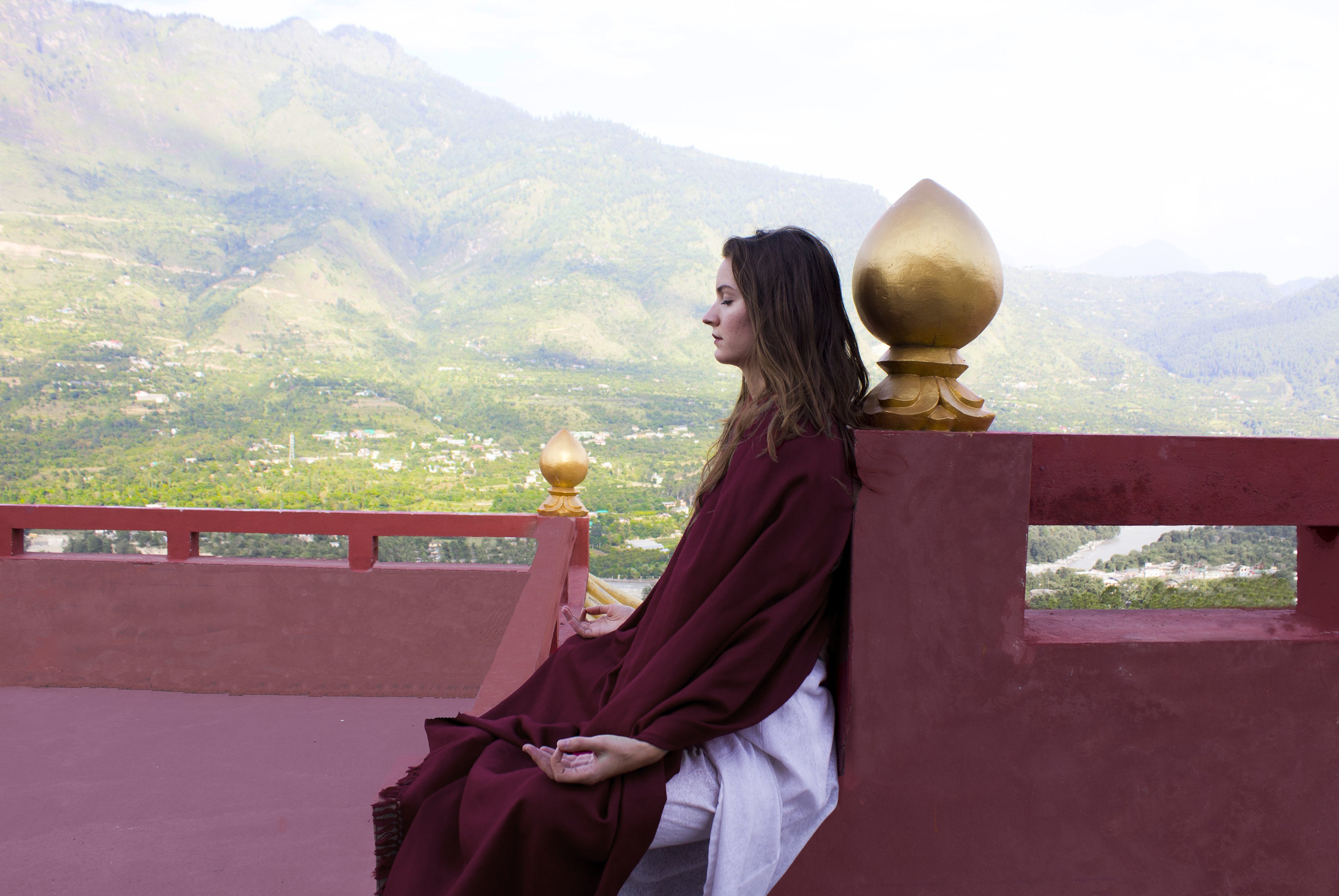 Close-up of a person in a burgundy shawl with a serene background of Himalayan mountains.