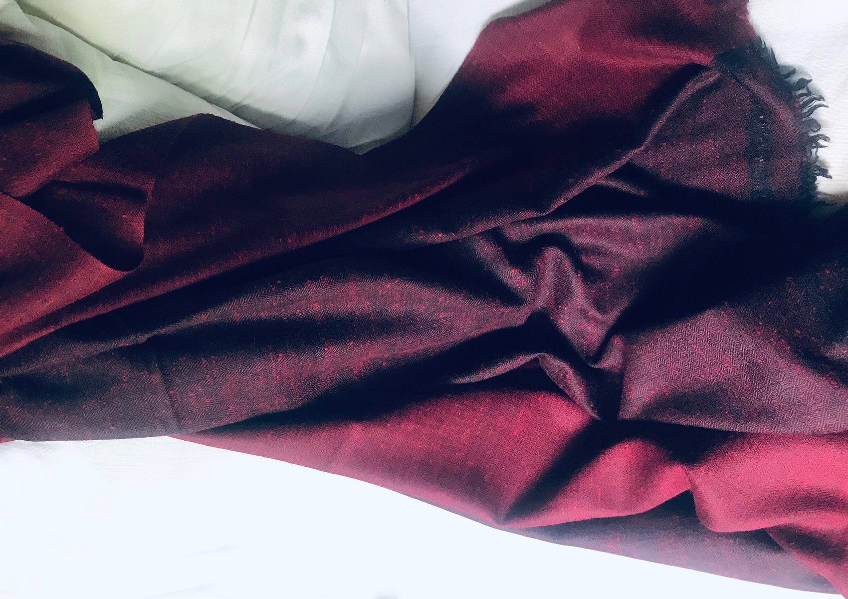 Close-up of a burgundy shawl laid out on a white surface, showcasing the soft fabric texture and deep color.