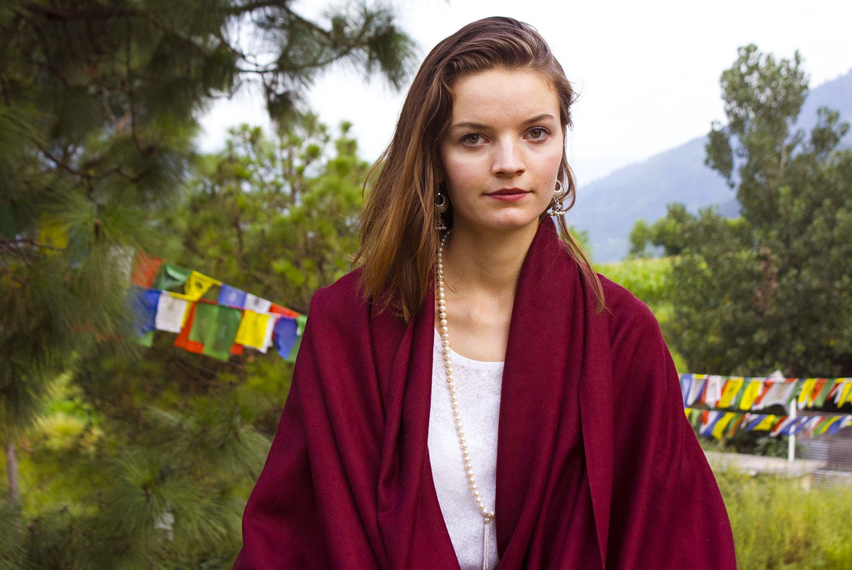 Woman meditating outdoors wrapped in a burgundy shawl, surrounded by nature, symbolizing peace.