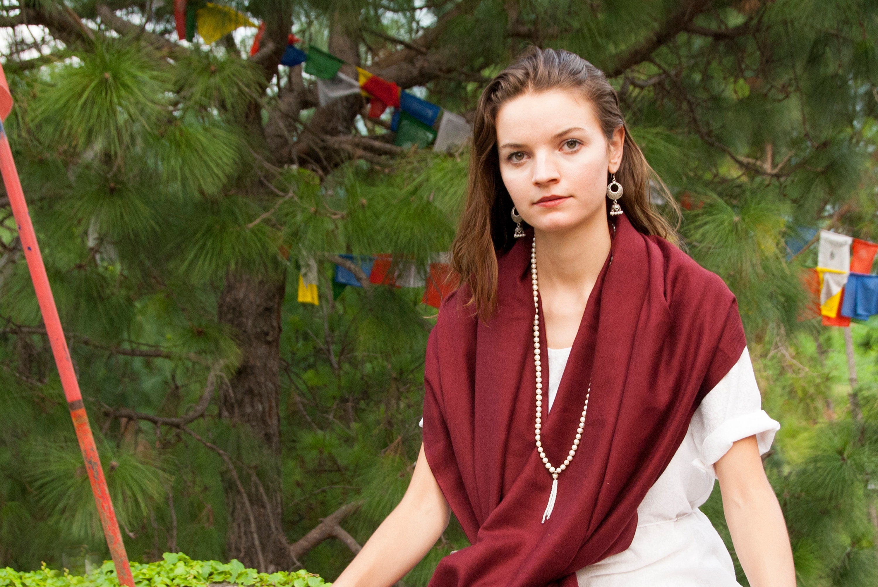 Young woman wearing a red shawl with colorful prayer flags in the background, evoking spirituality.