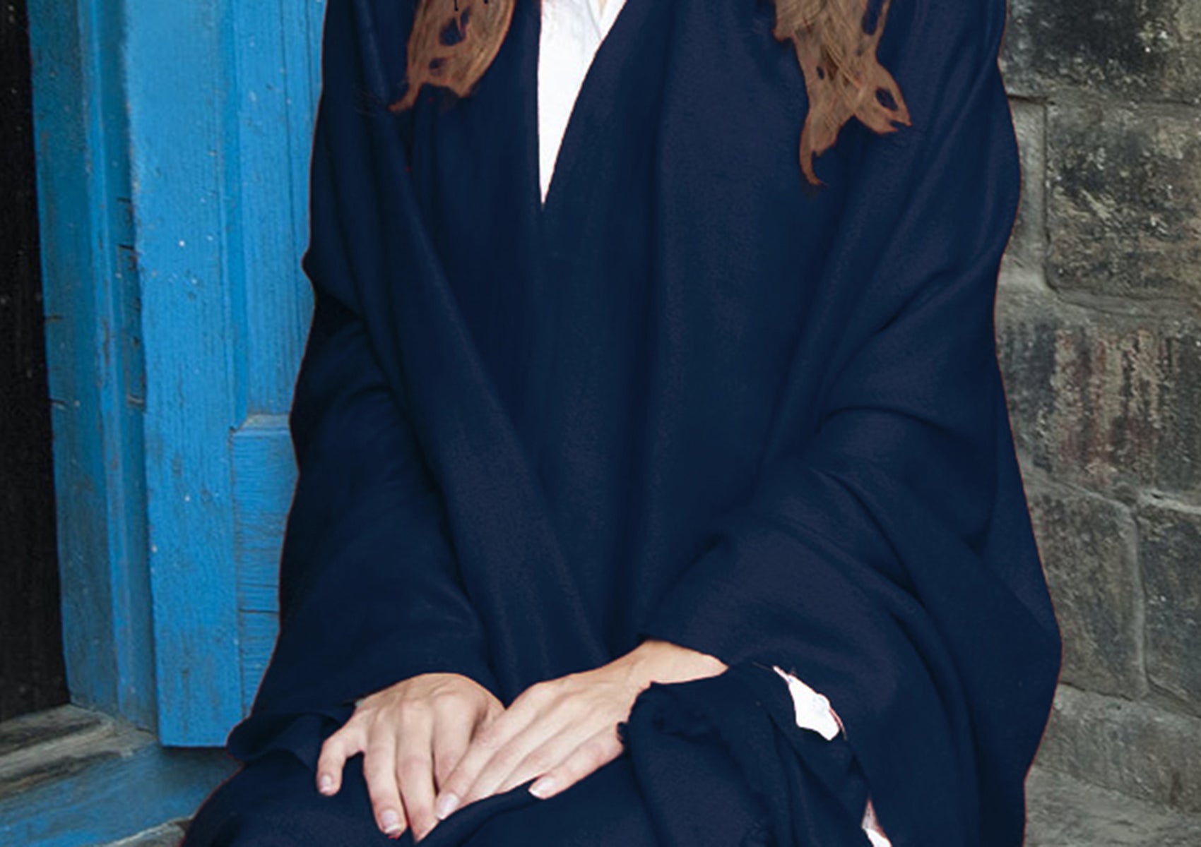 Close-up of a woman’s hands resting on her lap, wrapped in a navy blue pashmina shawl against a rustic blue door backdrop.