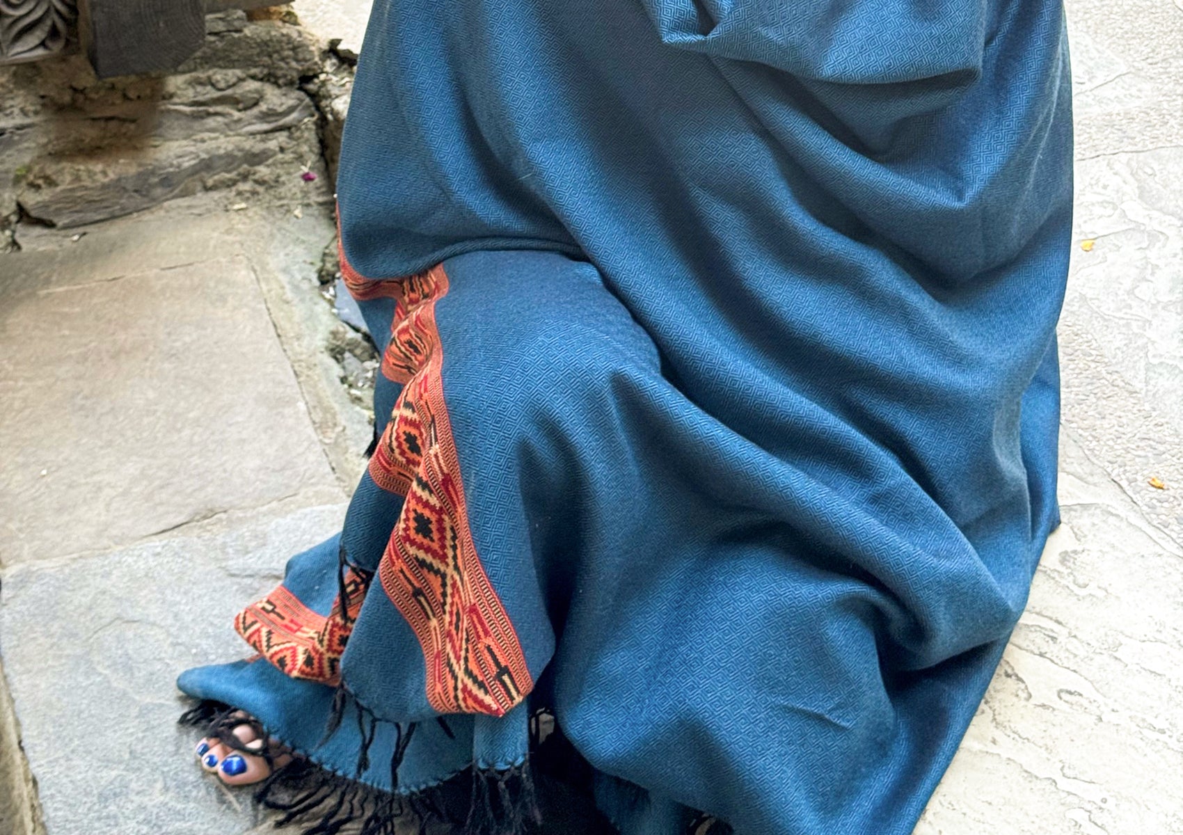 Closeup of a denim blue shawl draped elegantly, showcasing red and black woven accents along the edge