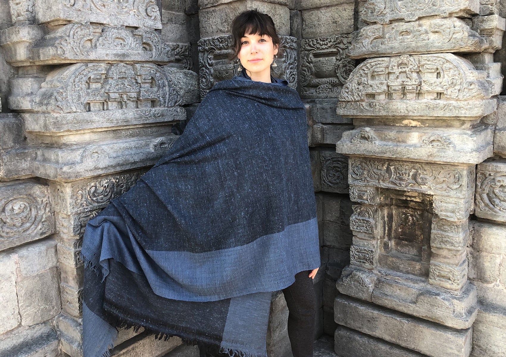 Blue shawl draped elegantly over a shoulder against a traditional stone-carved background.