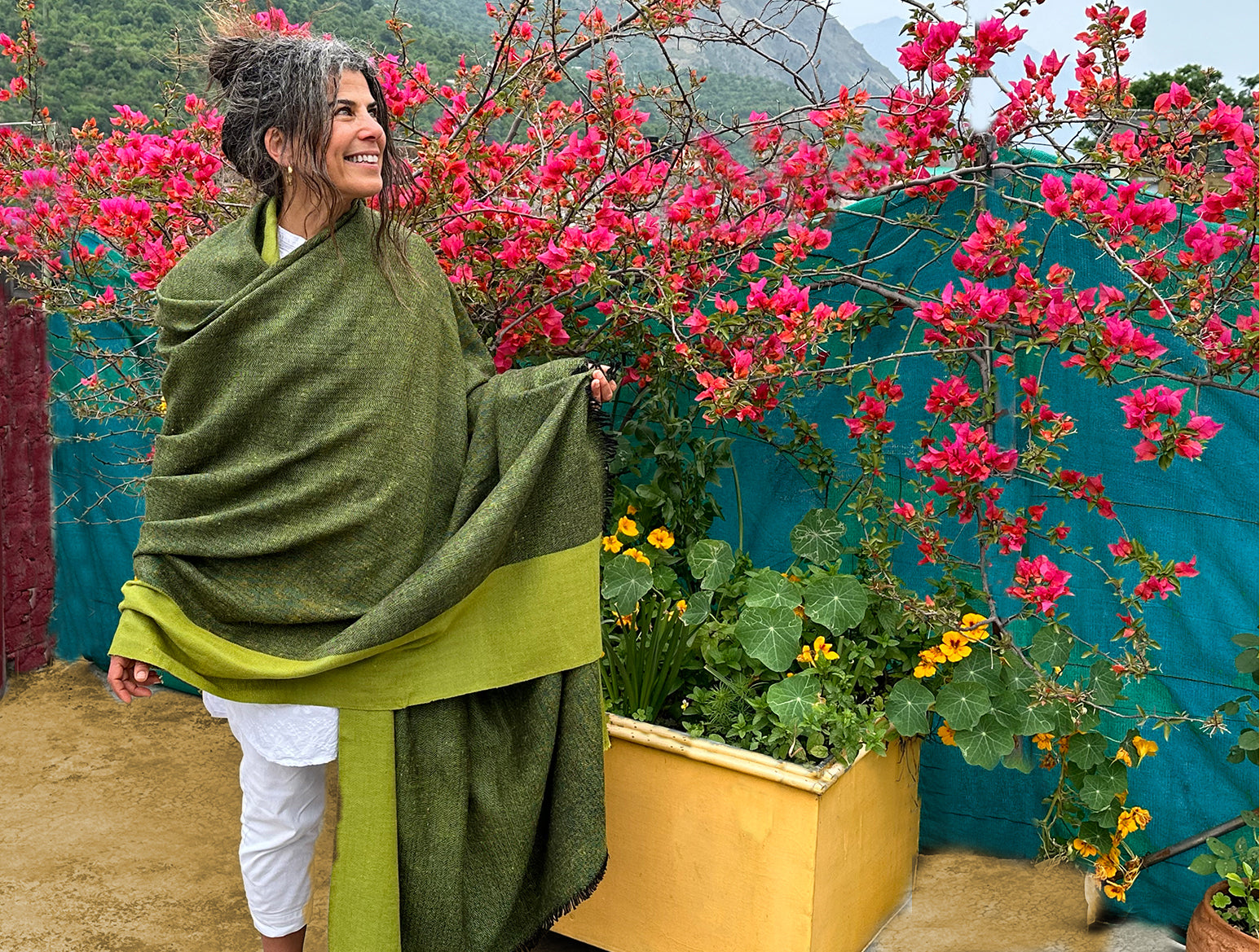 Green handwoven shawl draped on a woman, with vibrant flowers in the background.