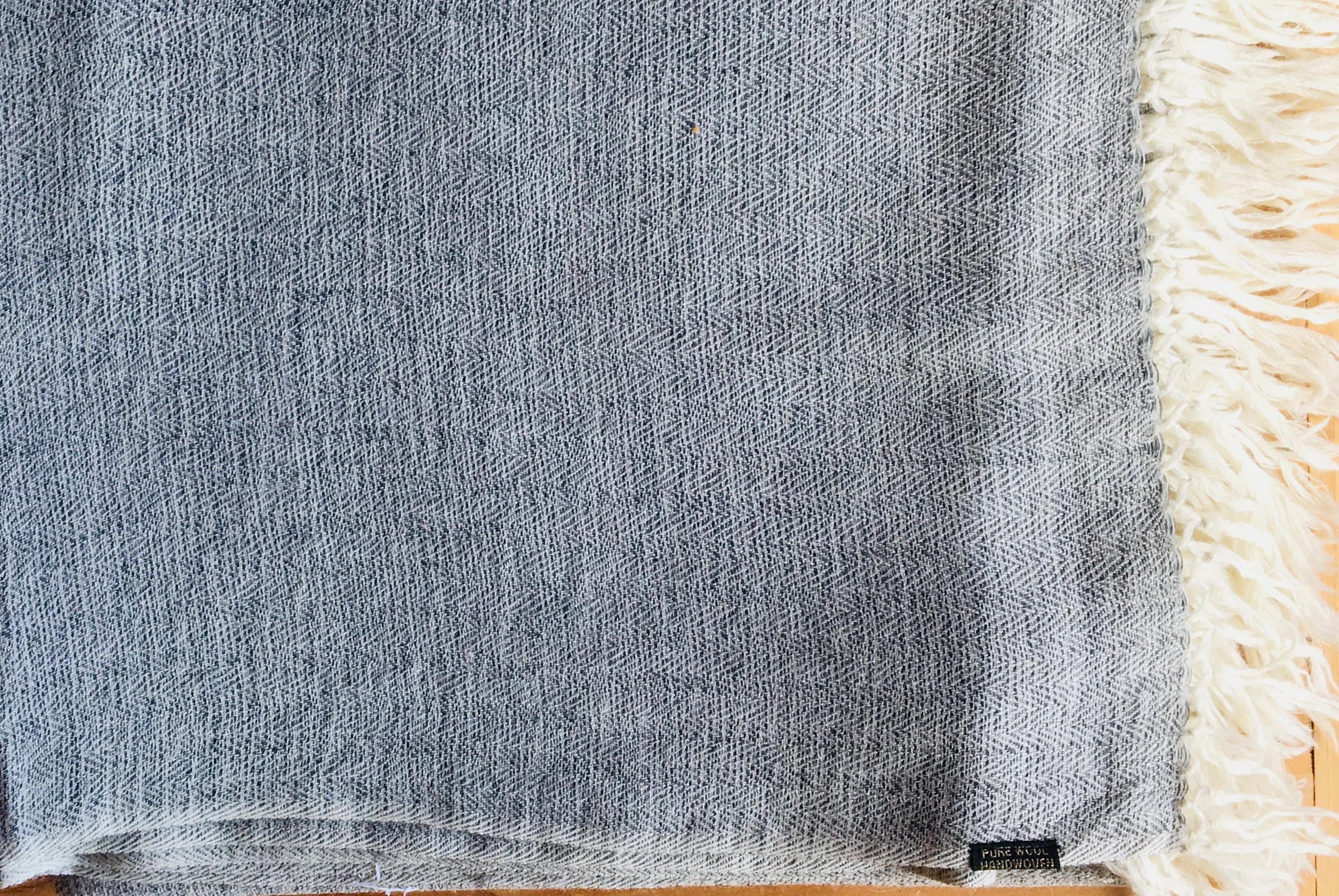 Close-up of a grey shawl with intricate fringes, showcasing the woven texture.