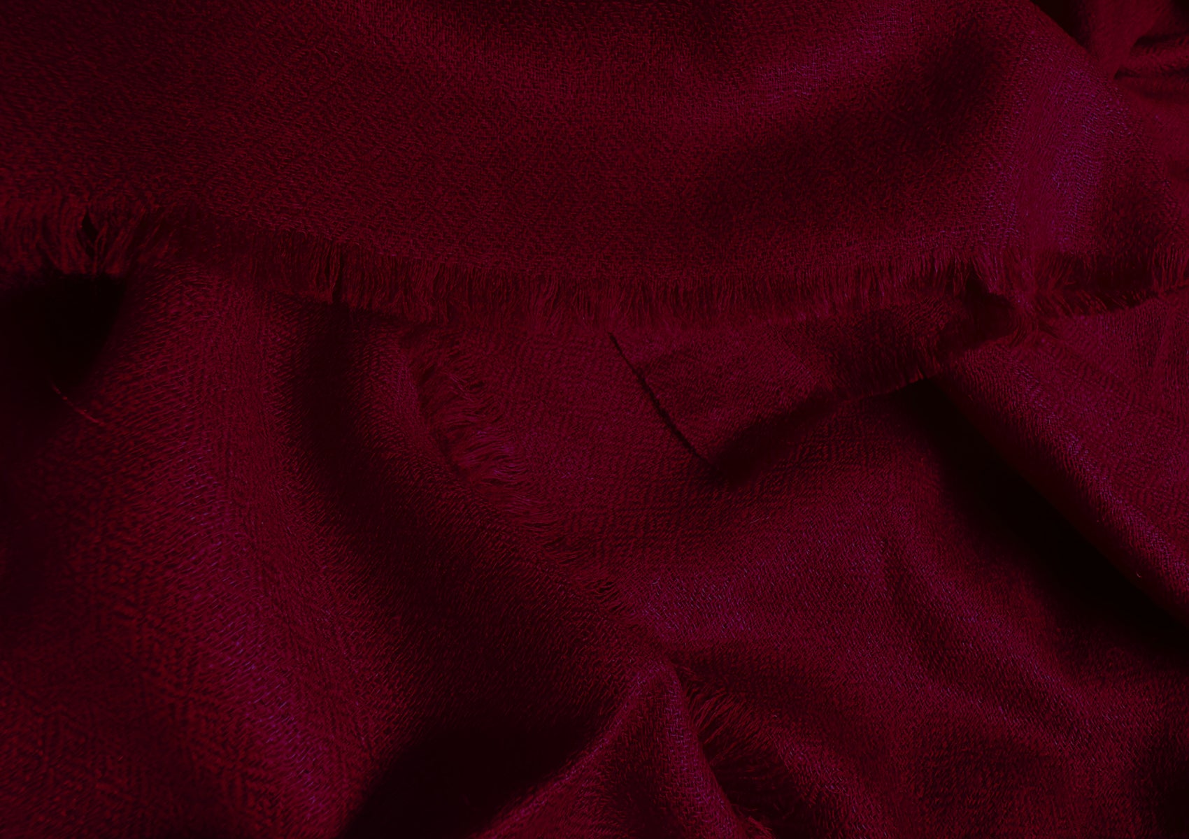 Close-up of a deep red Pashmina shawl with intricate diamond-pattern weaving and delicate fringed edges, highlighting its luxurious texture and craftsmanship.