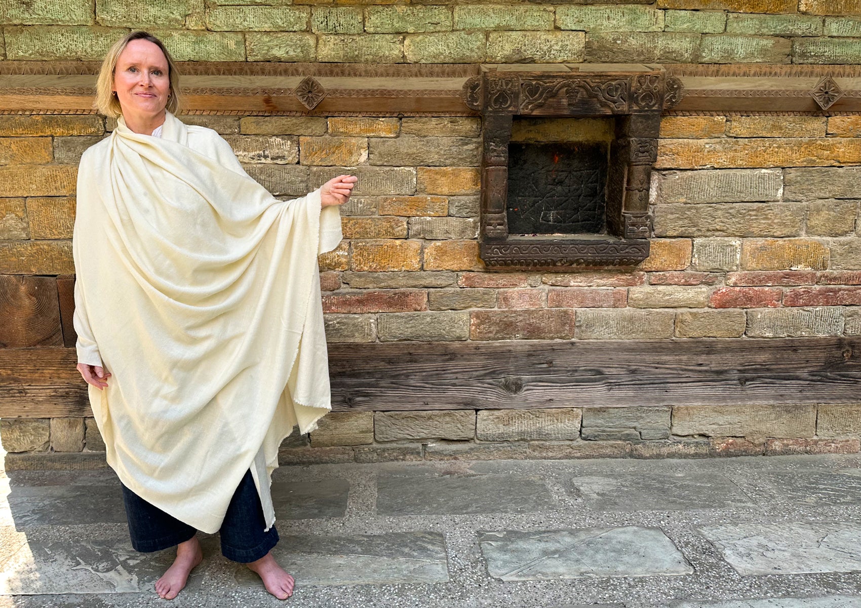 Person standing outdoors wrapped in a large cream angora shawl.