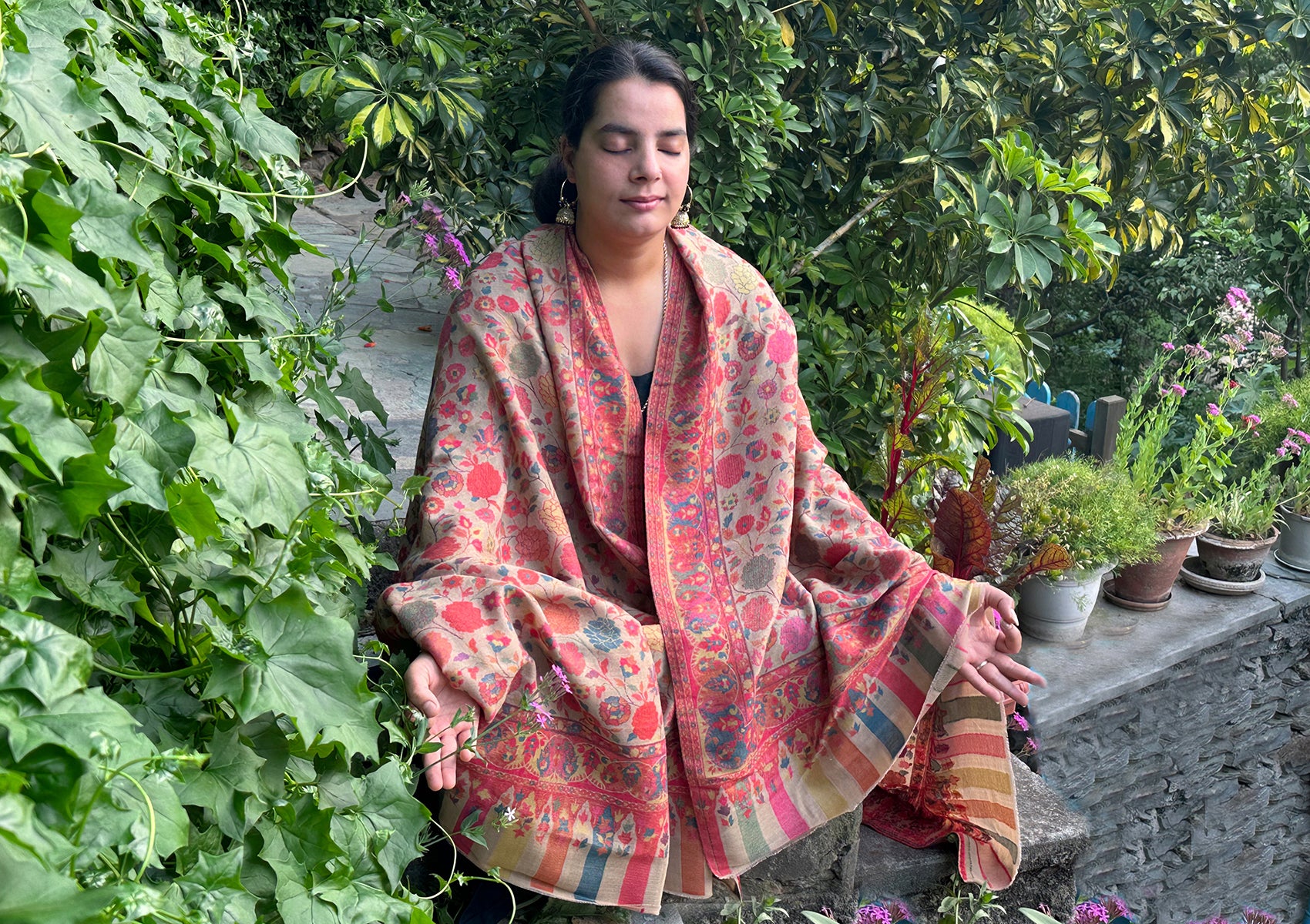 Individual meditating in a serene outdoor setting, draped in a beige floral Mohani Kani shawl, exuding peace and harmony amidst lush greenery.