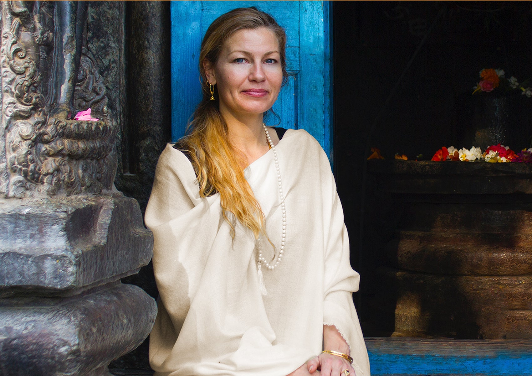 Woman draped in an elegant beige pashmina shawl, seated outside a traditional structure, expressing calmness.