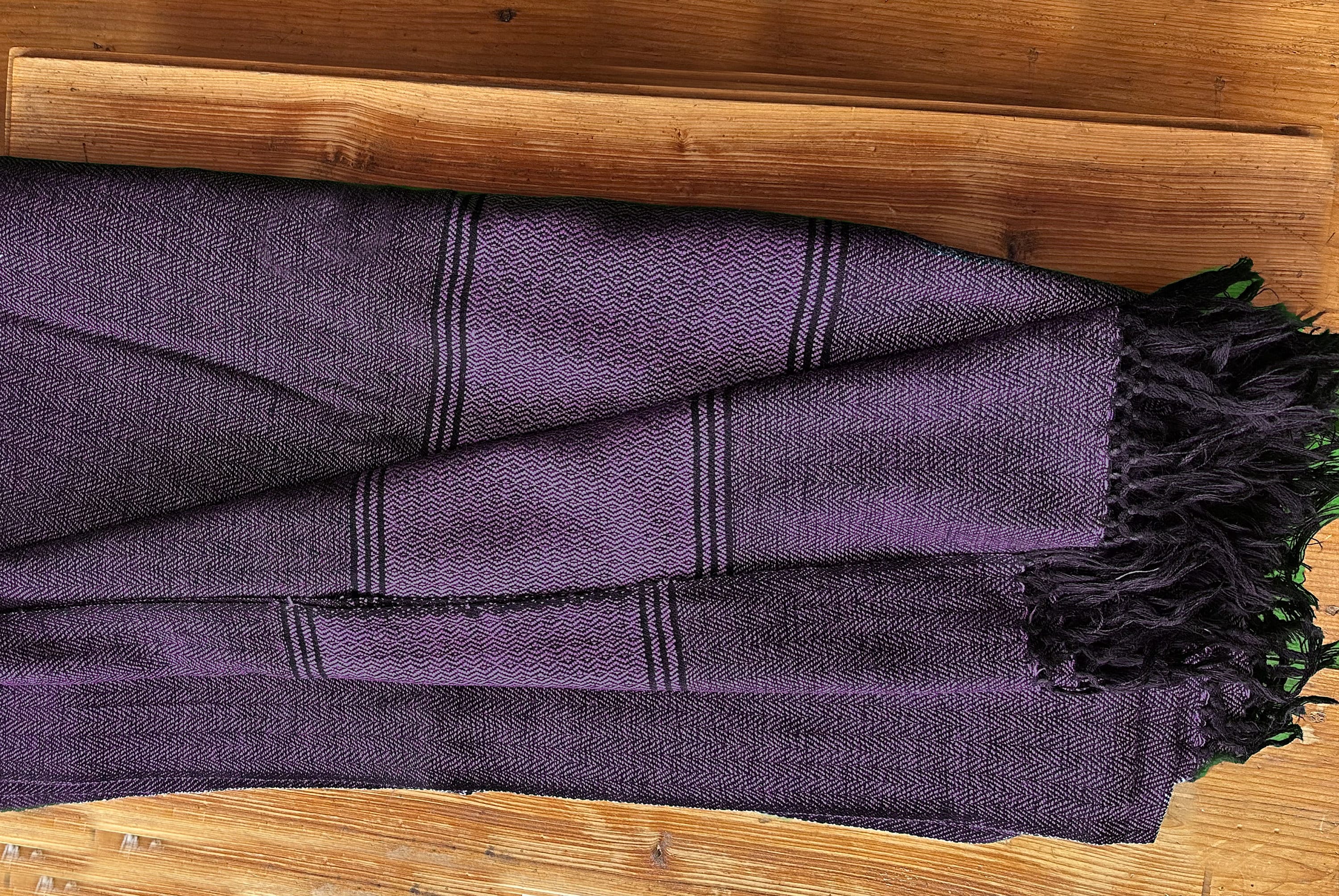 Purple Himalayan blanket folded and arranged on a wooden surface, showcasing its intricate weave.