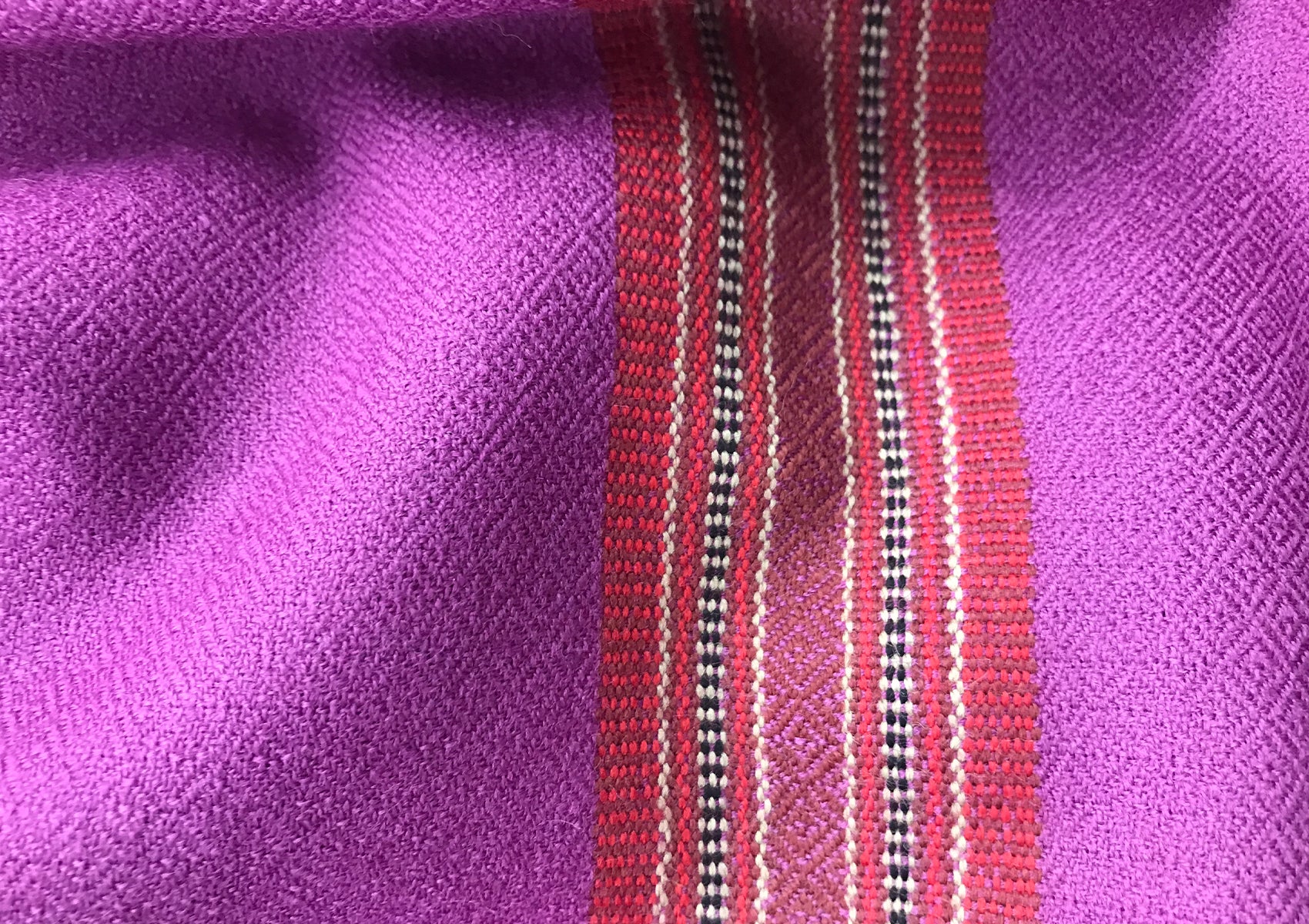 Close-up of a purple shawl with a colorful ethnic border featuring intricate red, black, and white woven patterns.