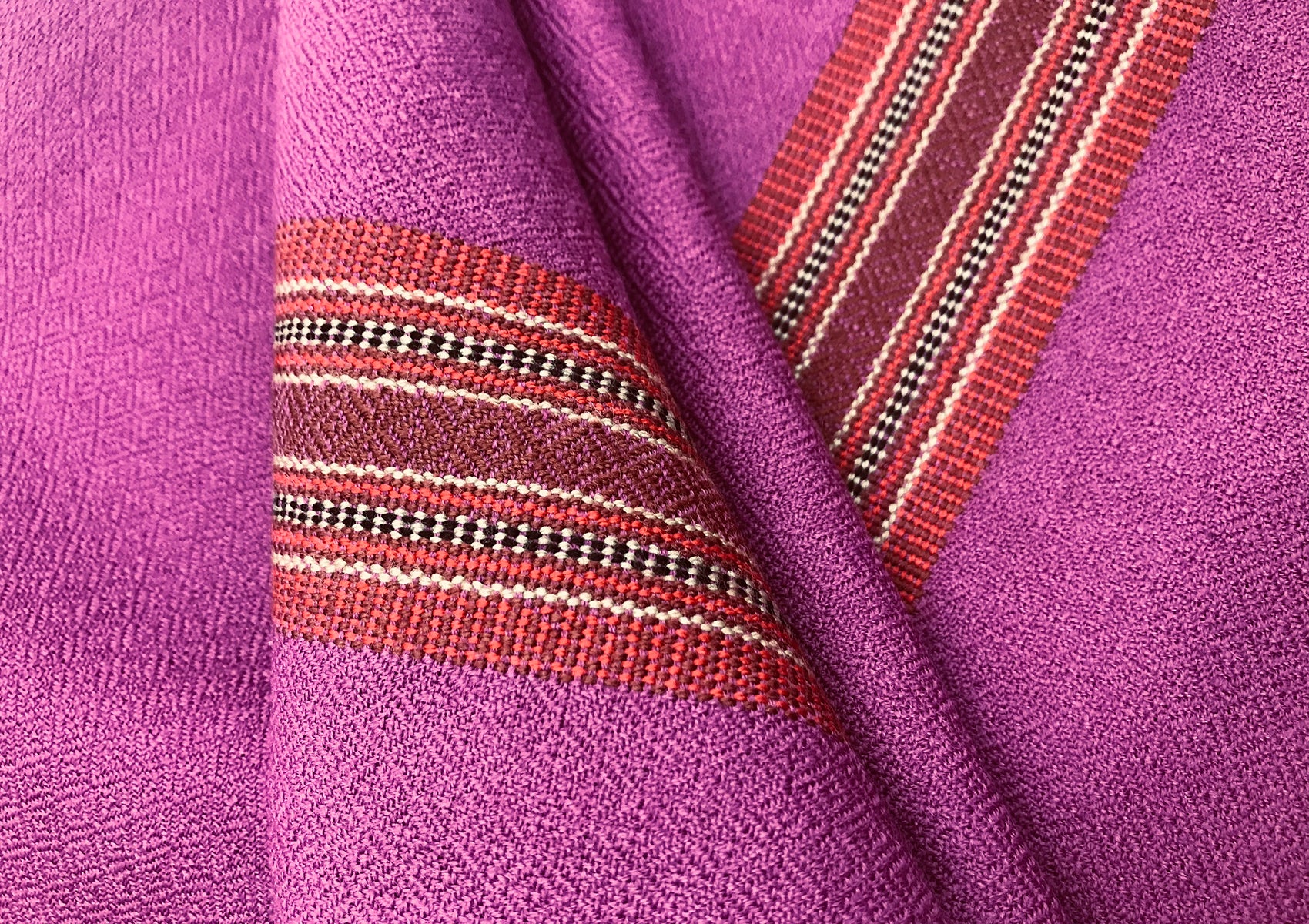 Detailed view of a purple shawl with a vibrant red and black ethnic border, showcasing intricate woven patterns and textured fabric