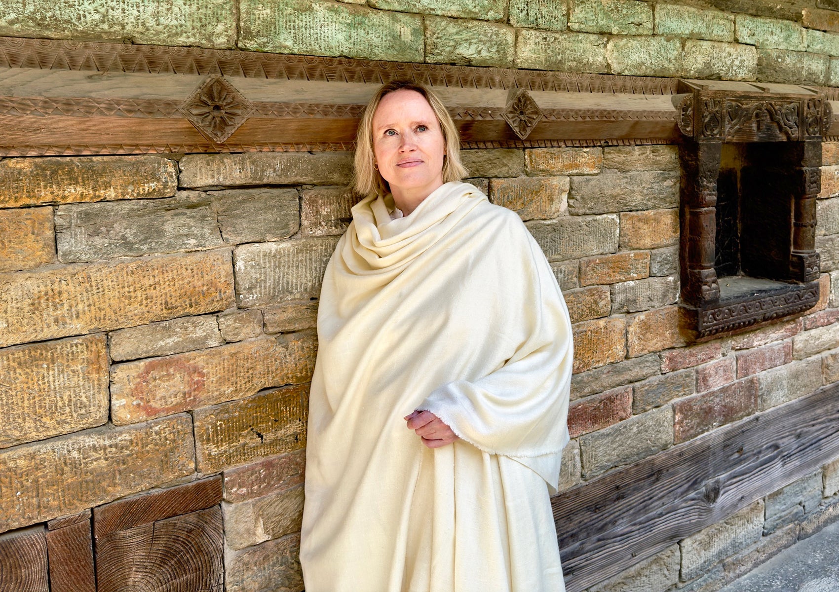 Elegant woman with angora prayer shawl against a rustic stone wall.