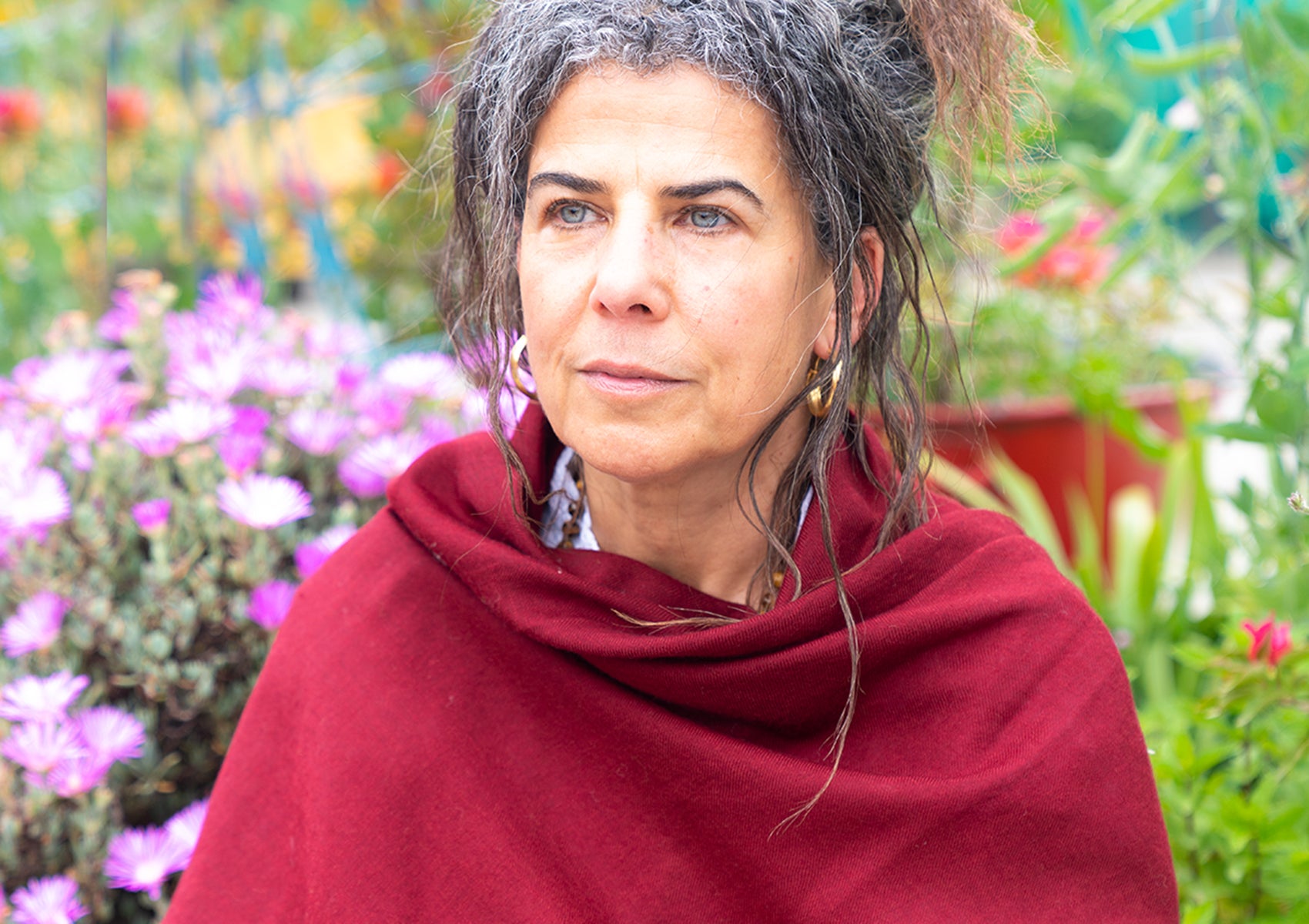 A close-up of a red shawl with embroidered Om symbols, surrounded by purple flowers, creating a serene setting.