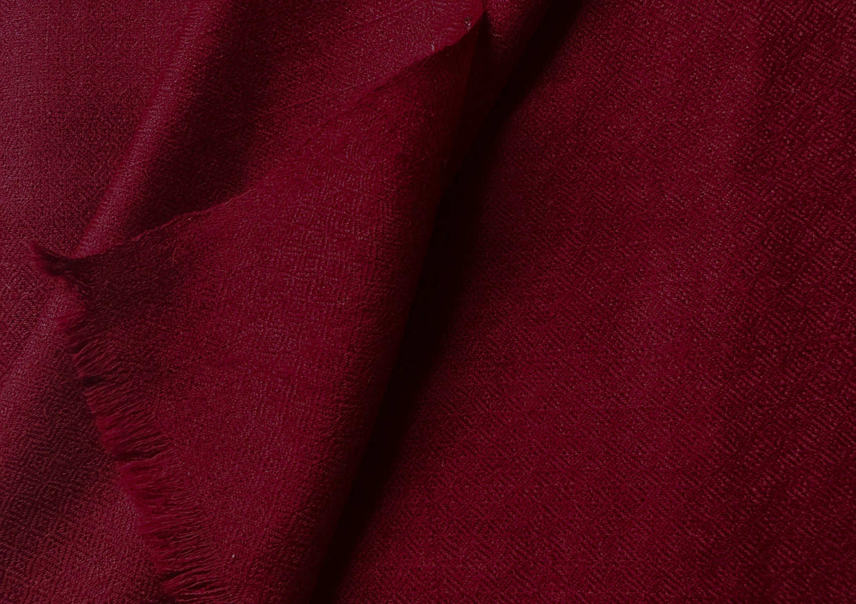 Red wool shawl folded on a rustic wooden surface, showcasing the luxurious material.