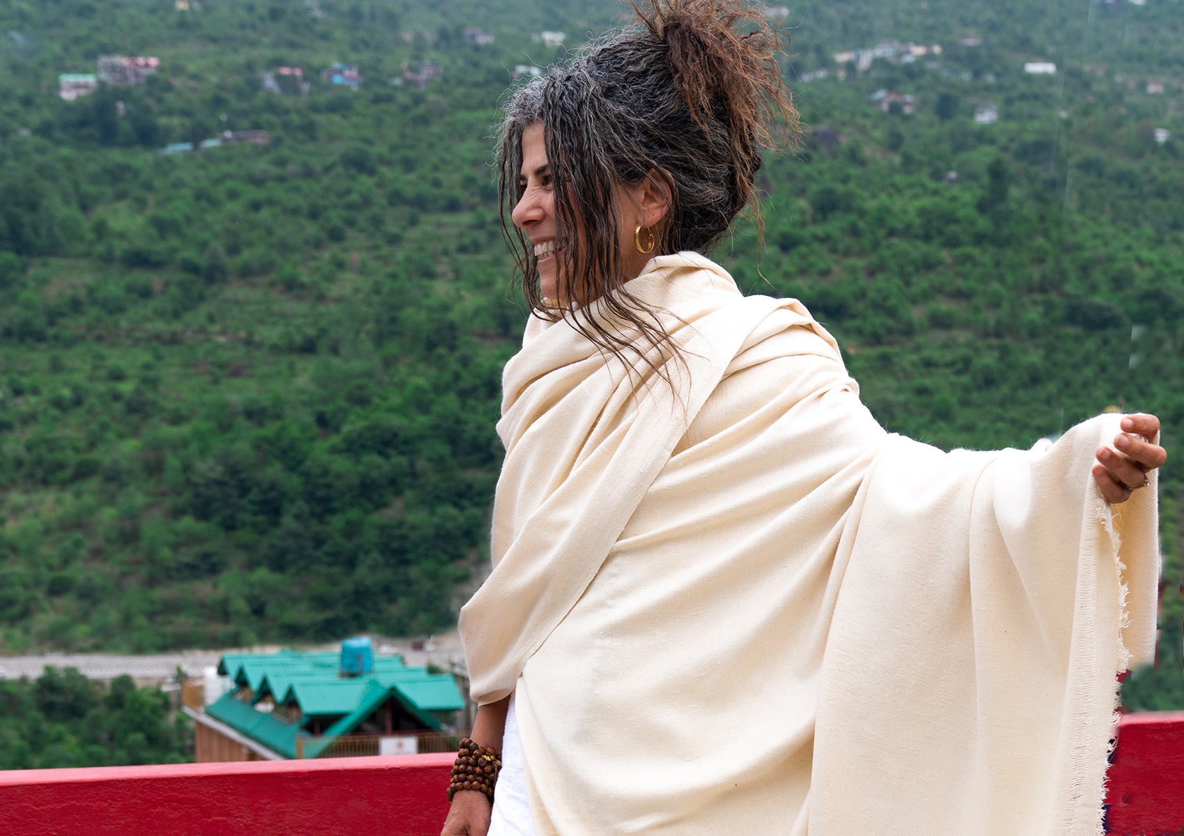 This image presents an elegant cream silk shawl gracefully wrapped around the model, with a lush green valley backdrop, enhancing its serene appeal.