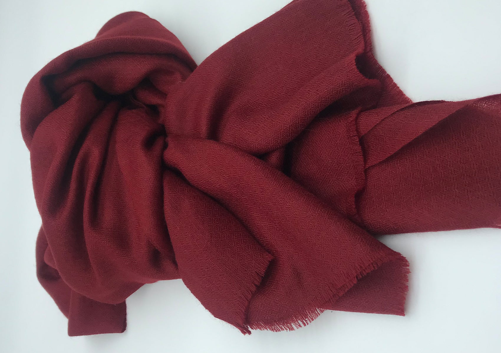 Soft deep red pashmina shawl elegantly folded, highlighting the intricate texture of the fabric on a white background.