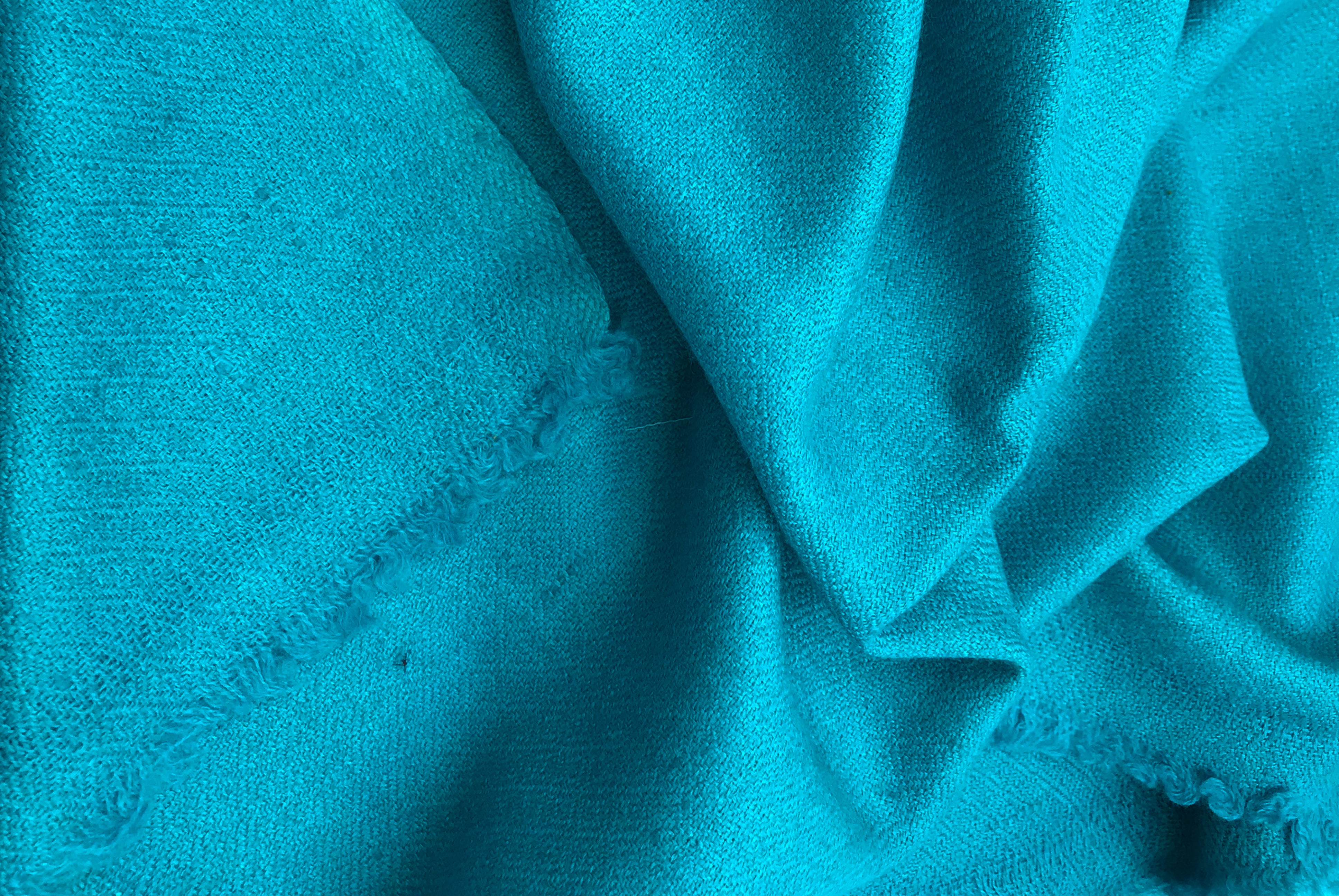 Detailed view of a turquoise silk pashmina shawl folded at the corner, showcasing its fine texture and cozy feel.