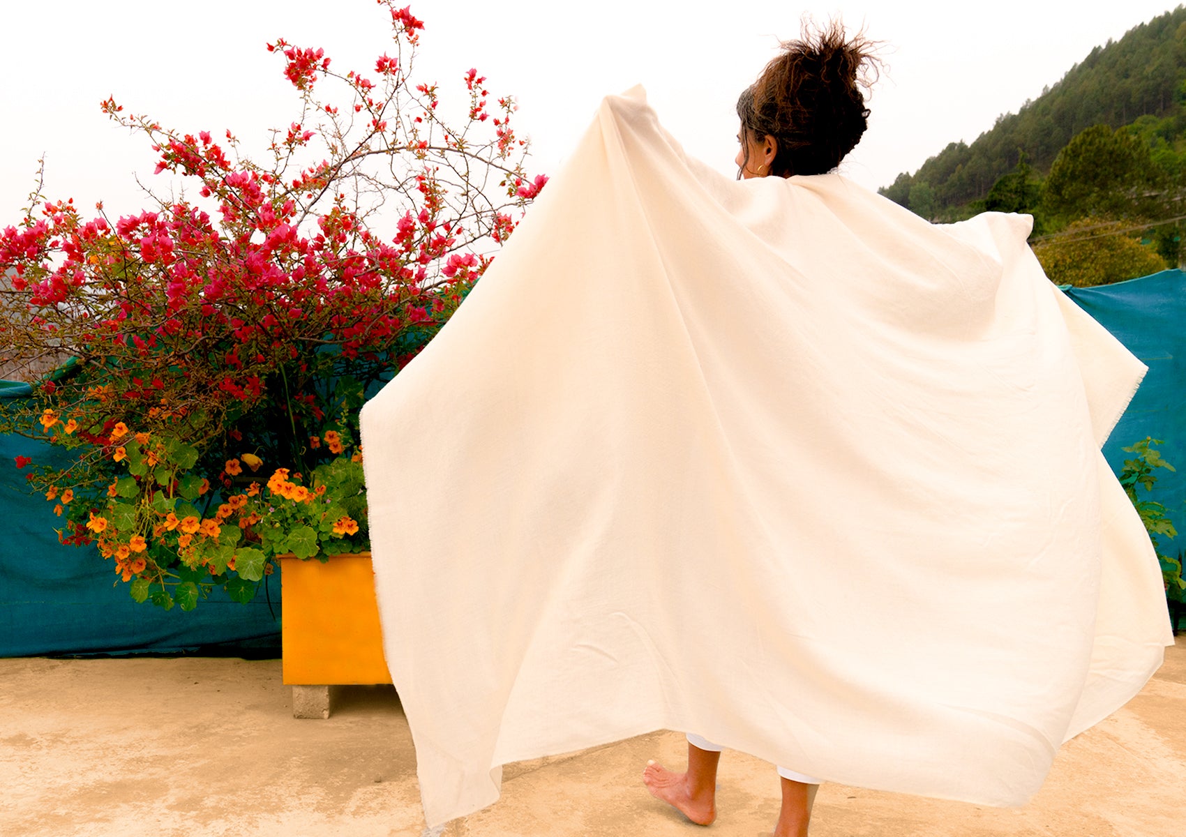 A large white merino wool shawl held against a background of flowers, capturing elegance and simplicity.