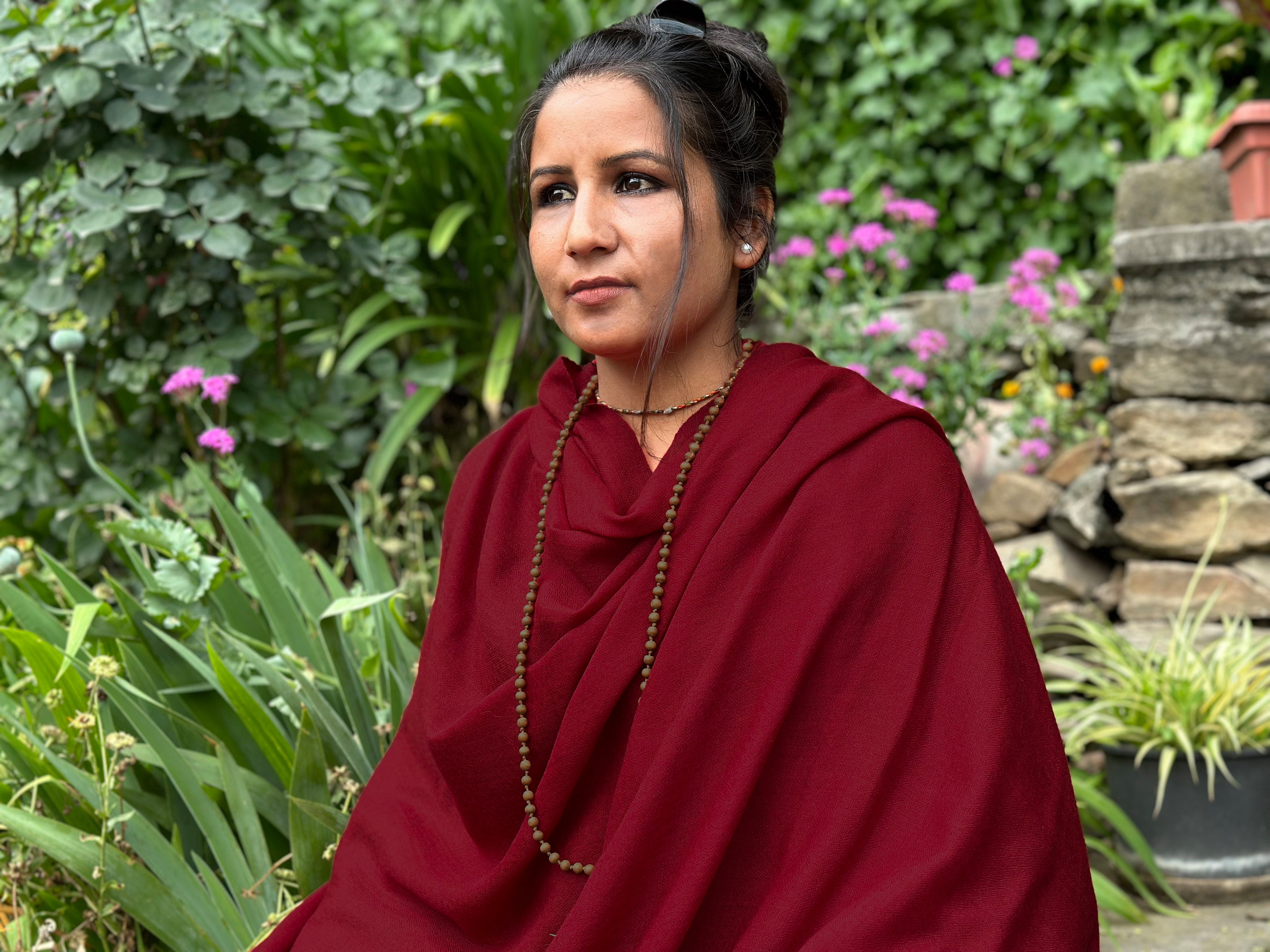 Woman wearing a red shawl, enjoying a natural setting with red flowers around her, signifying peace and harmony.