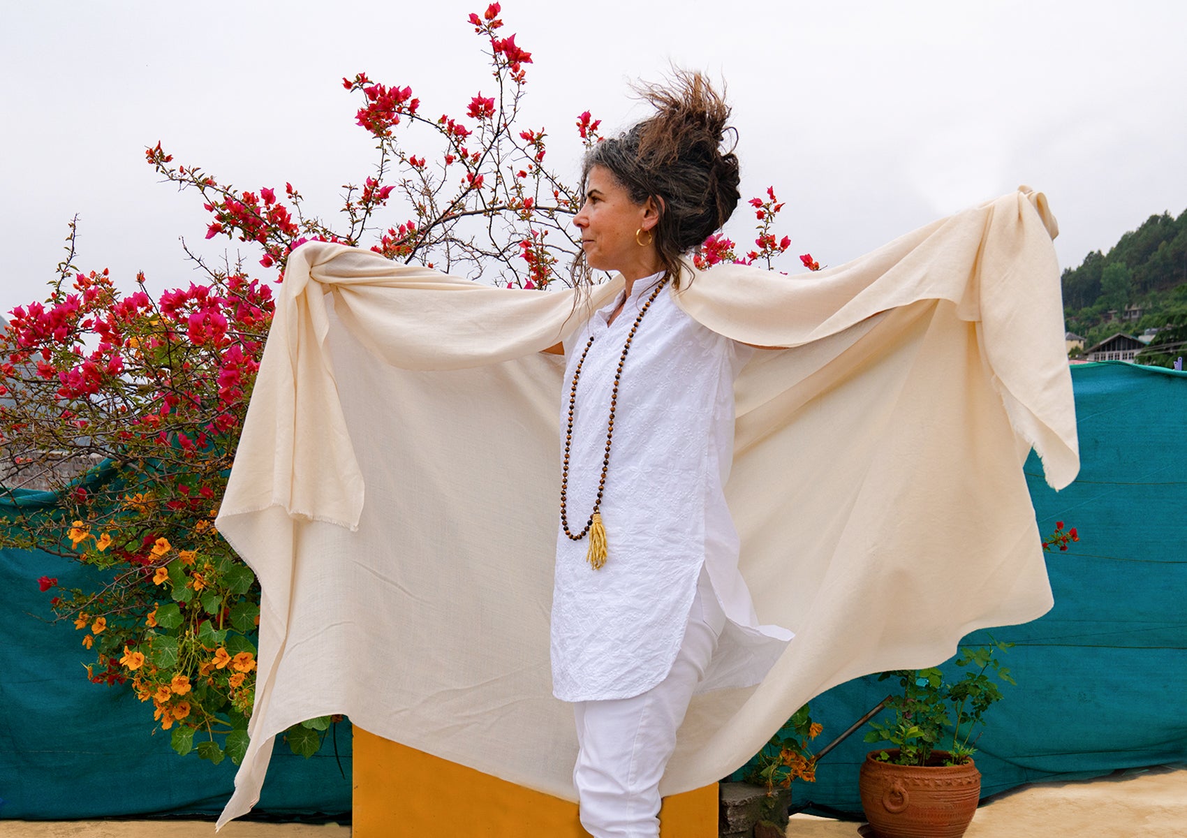 Woman wearing a white shawl, enjoying a natural setting with red flowers around her, signifying peace and harmony.