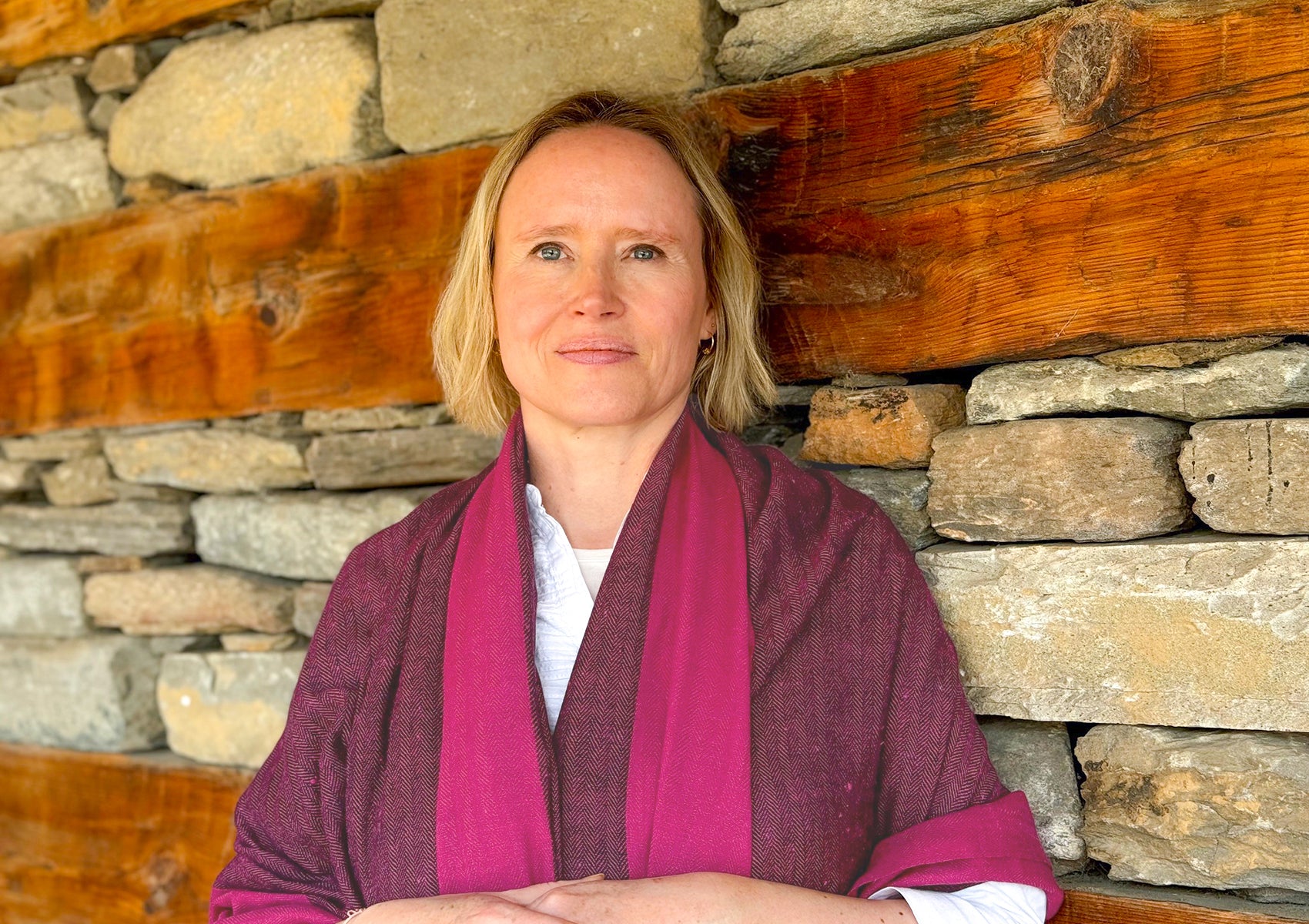 Woman standing in front of a rustic stone wall, wearing a magenta meditation shawl, exuding calm and serenity.