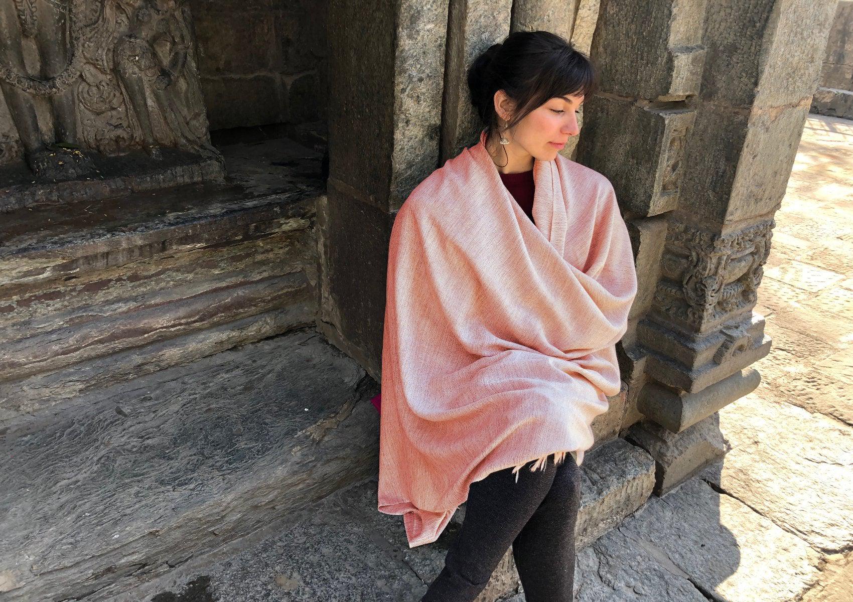 Woman wrapped in a pink shawl standing next to an ancient stone background, exuding a calm vibe.