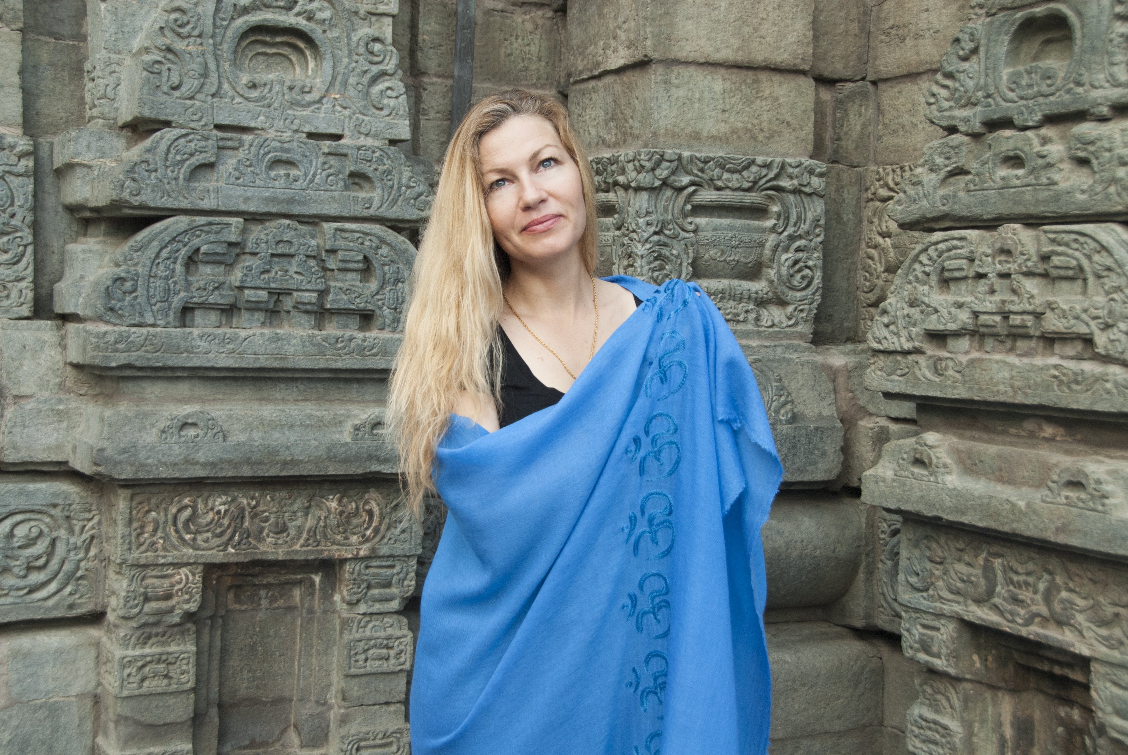 Woman wearing a blue shawl standing against ancient stone temple walls.