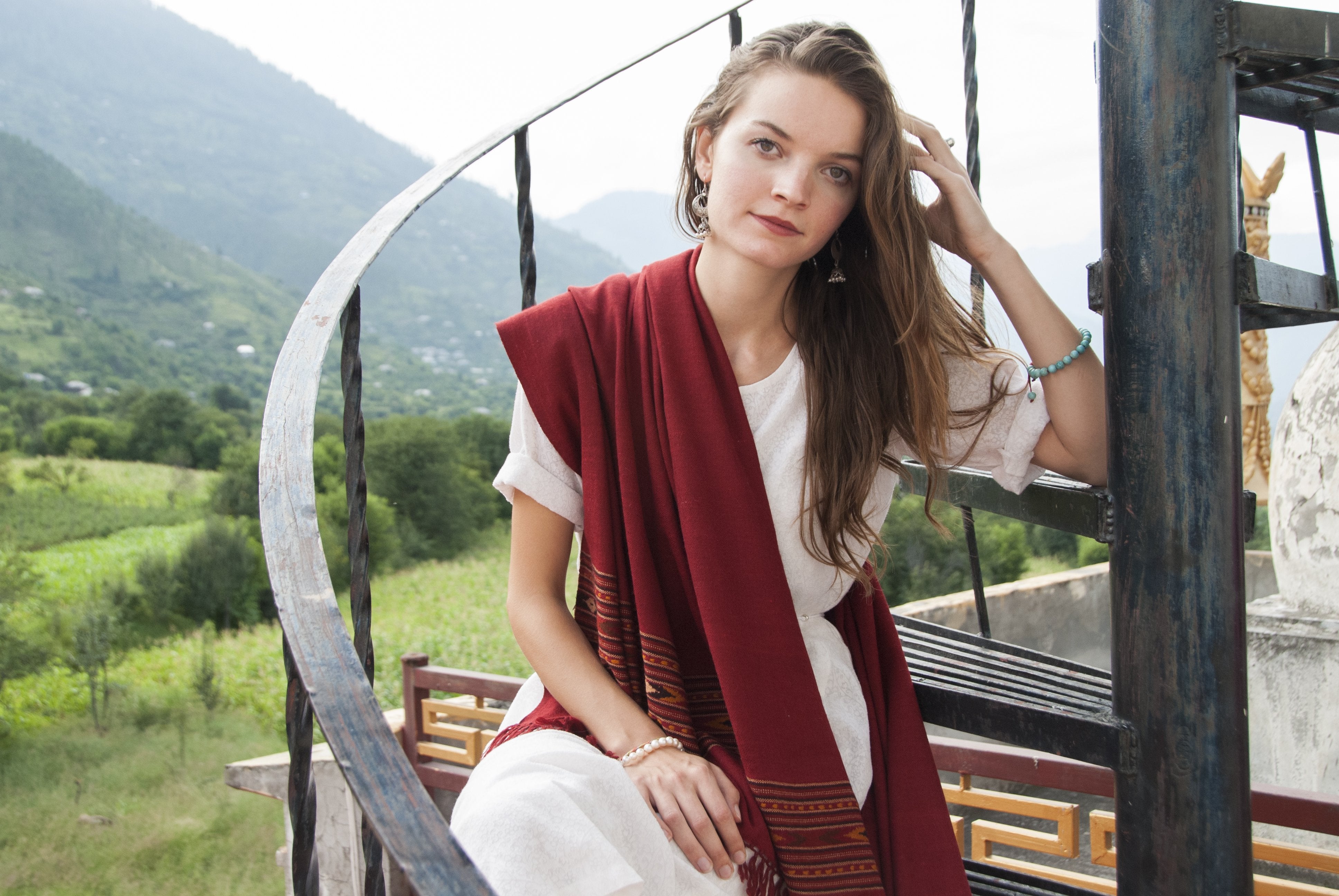 Burgundy red meditation shawl draped over a woman’s shoulder, with detailed temple architecture in the background.