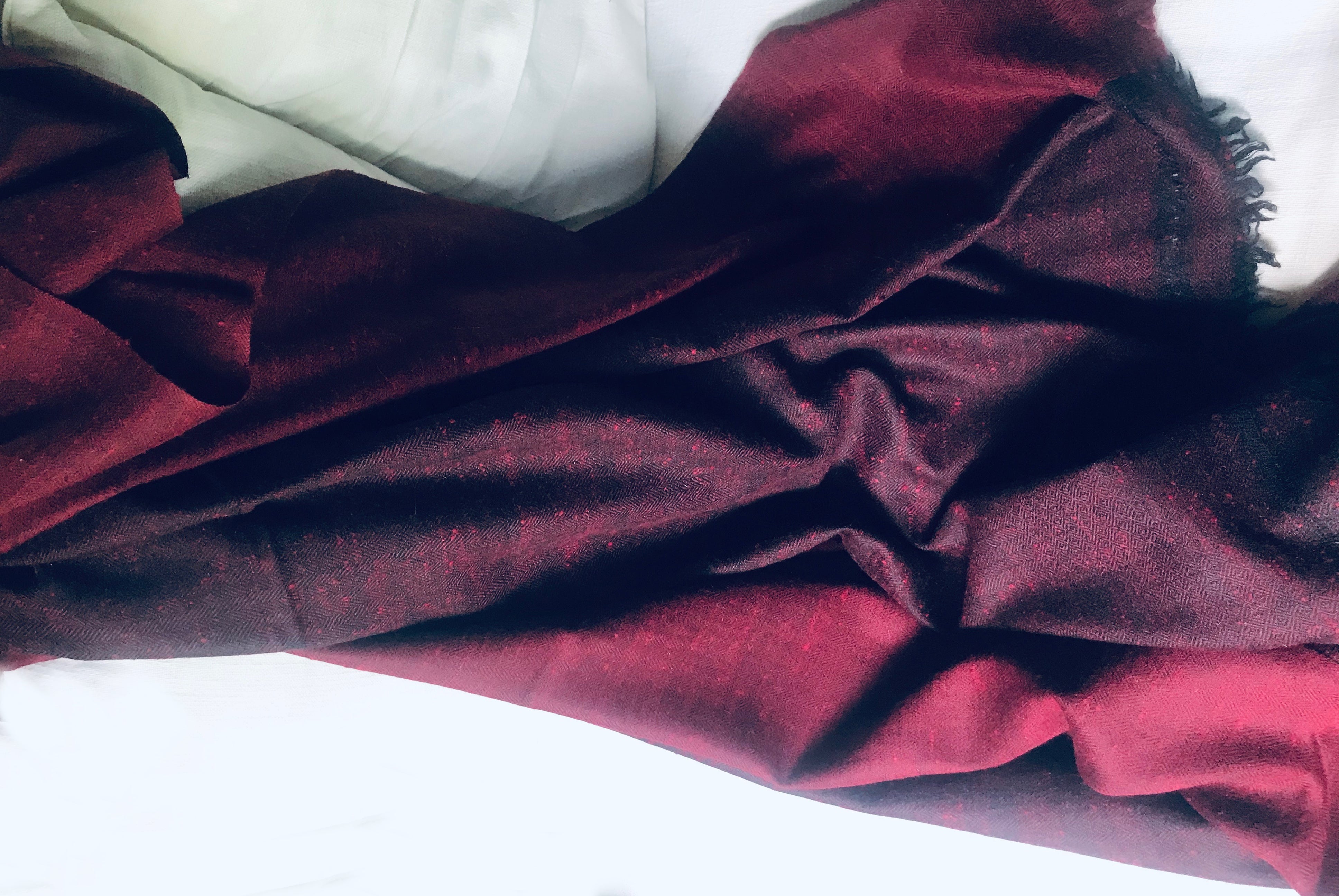 Burgundy shawl laid out on a white bed, showing its softness and texture.