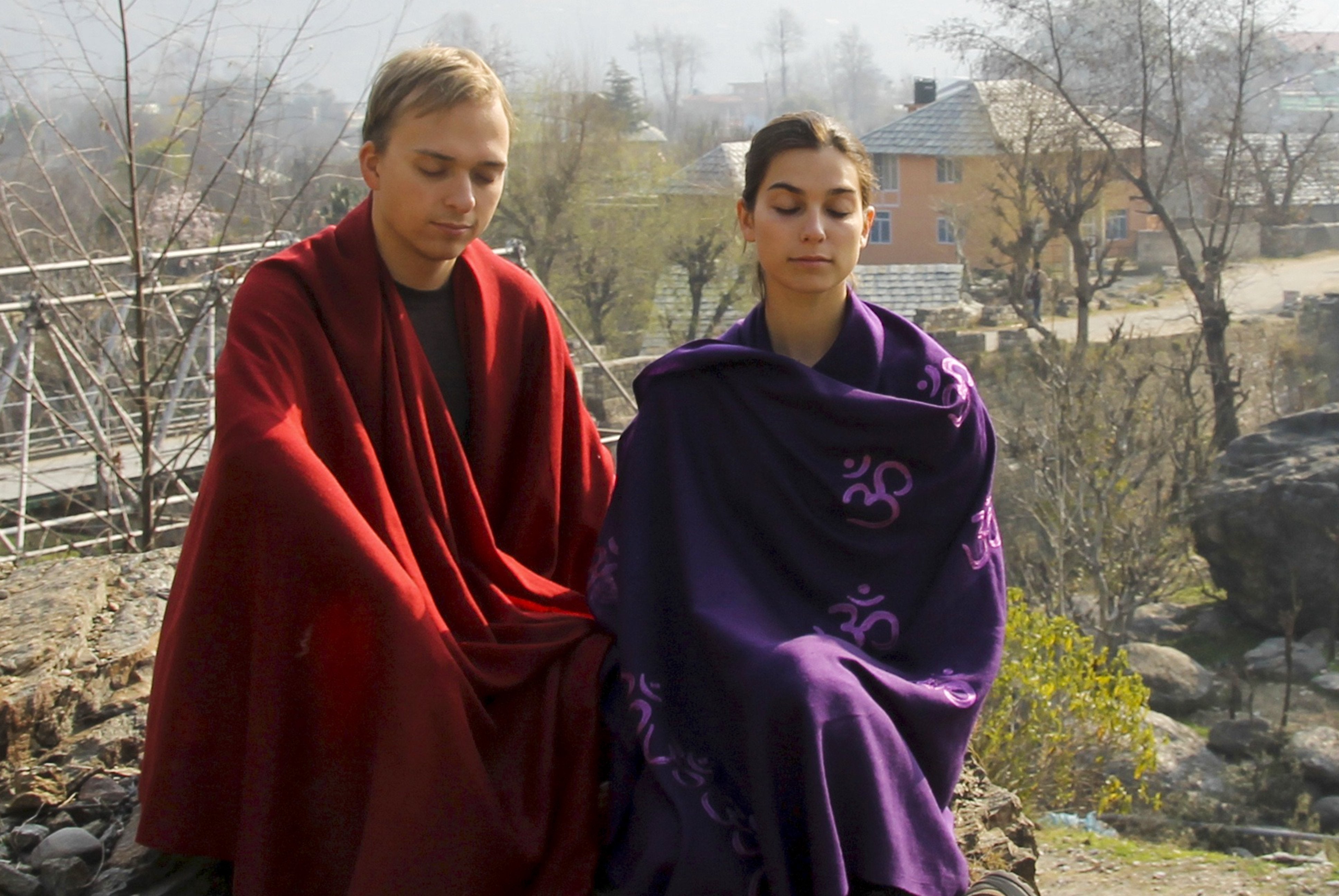 Man and woman meditating outdoors with red and purple shawls.