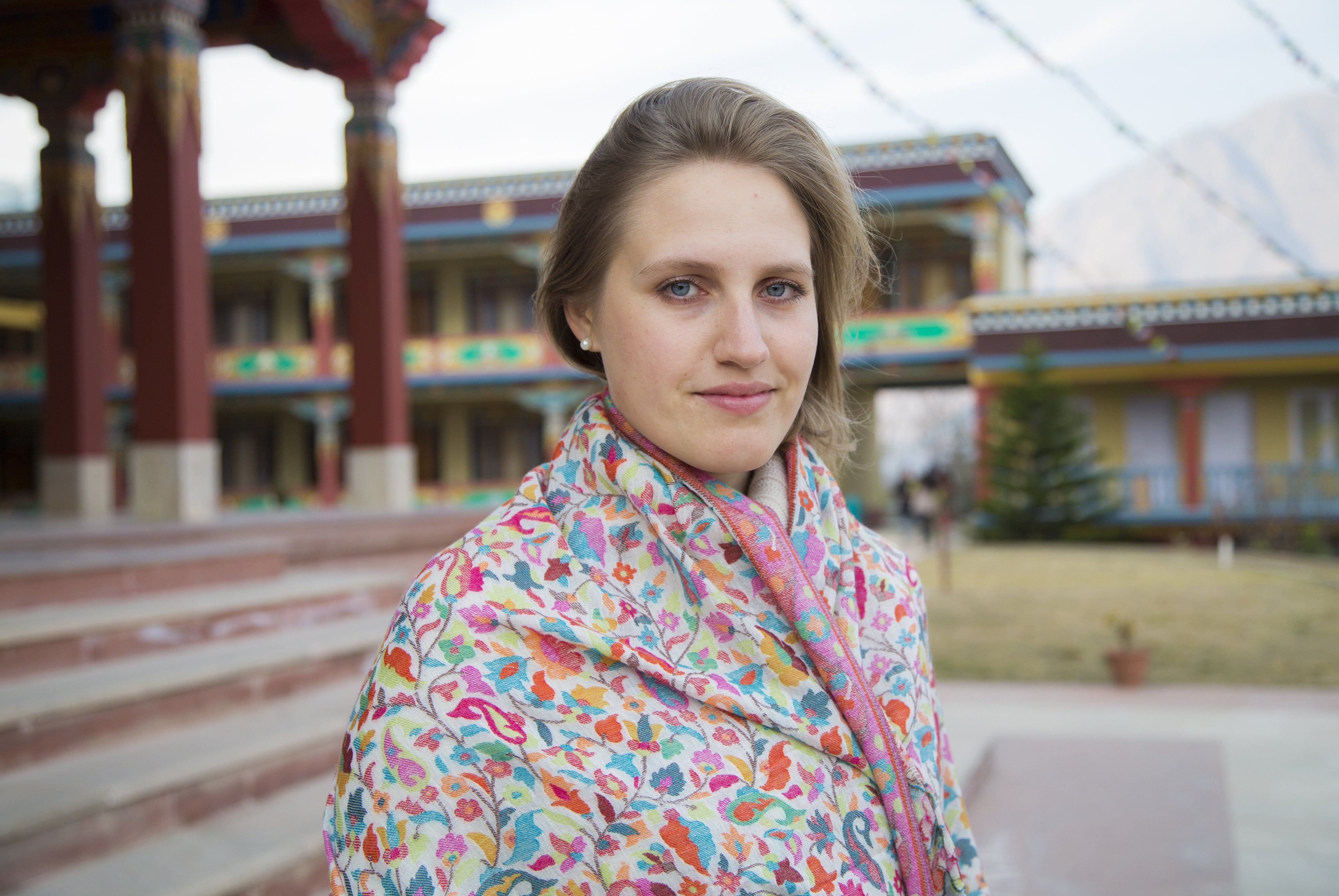 Woman posing with cream-colored Kani shawl in a lush setting.