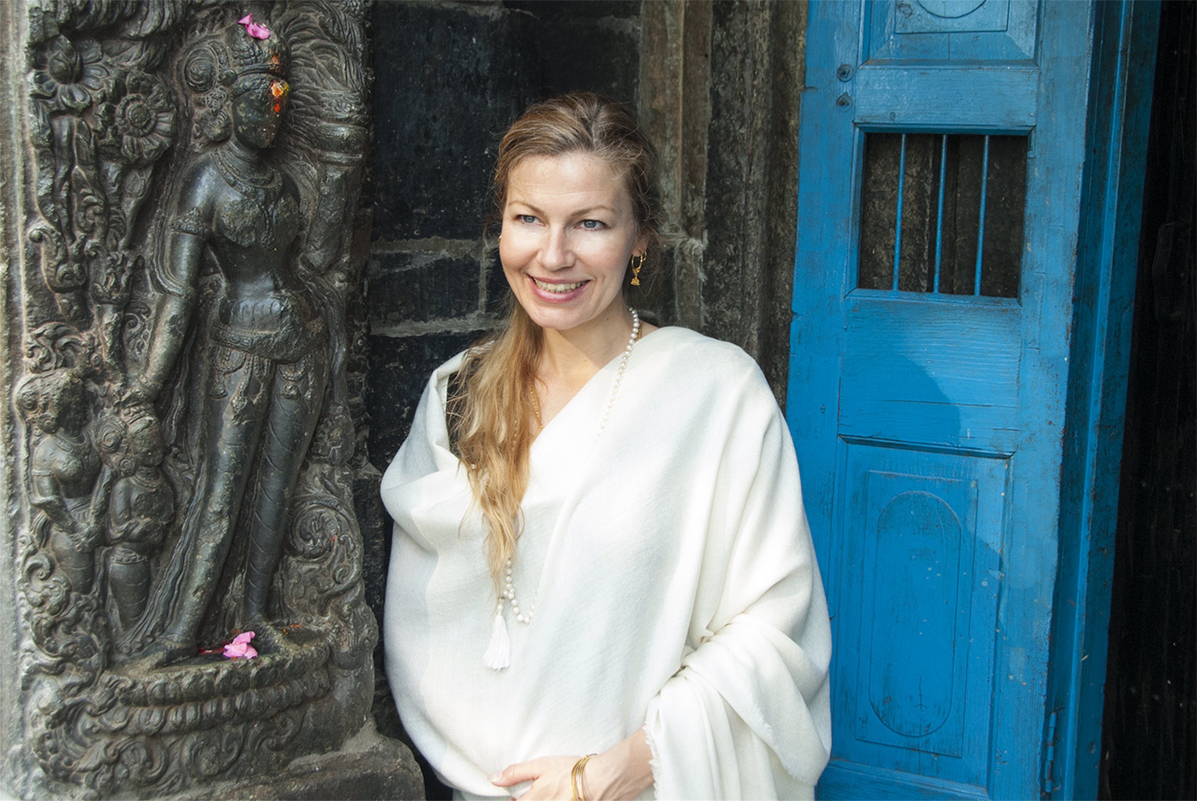 Close-up of a woman wearing a cream meditation shawl, standing against a temple wall with a serene expression.