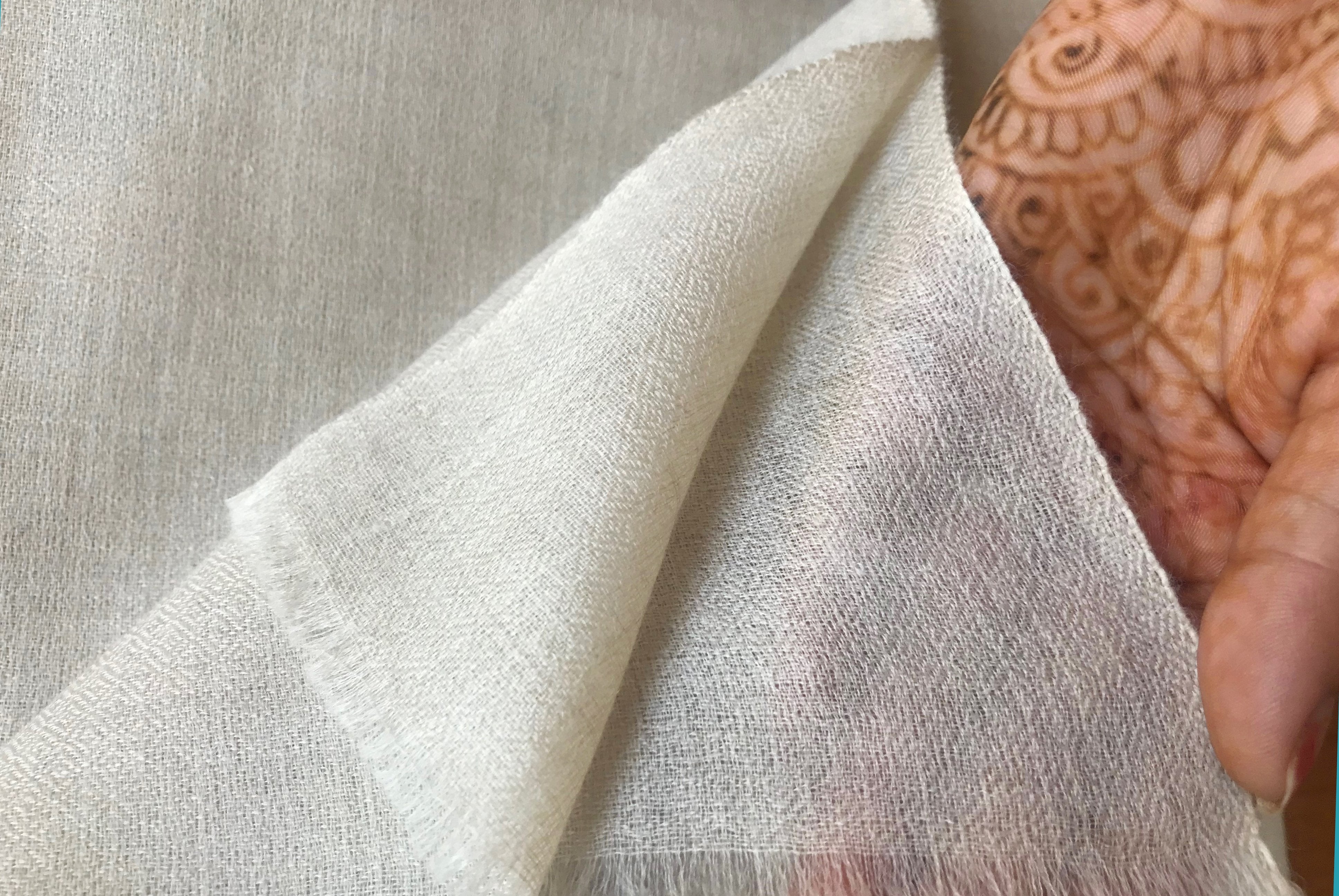 Close-up of a cream pashmina shawl, showing the delicate fabric weave held in a hand with henna designs.