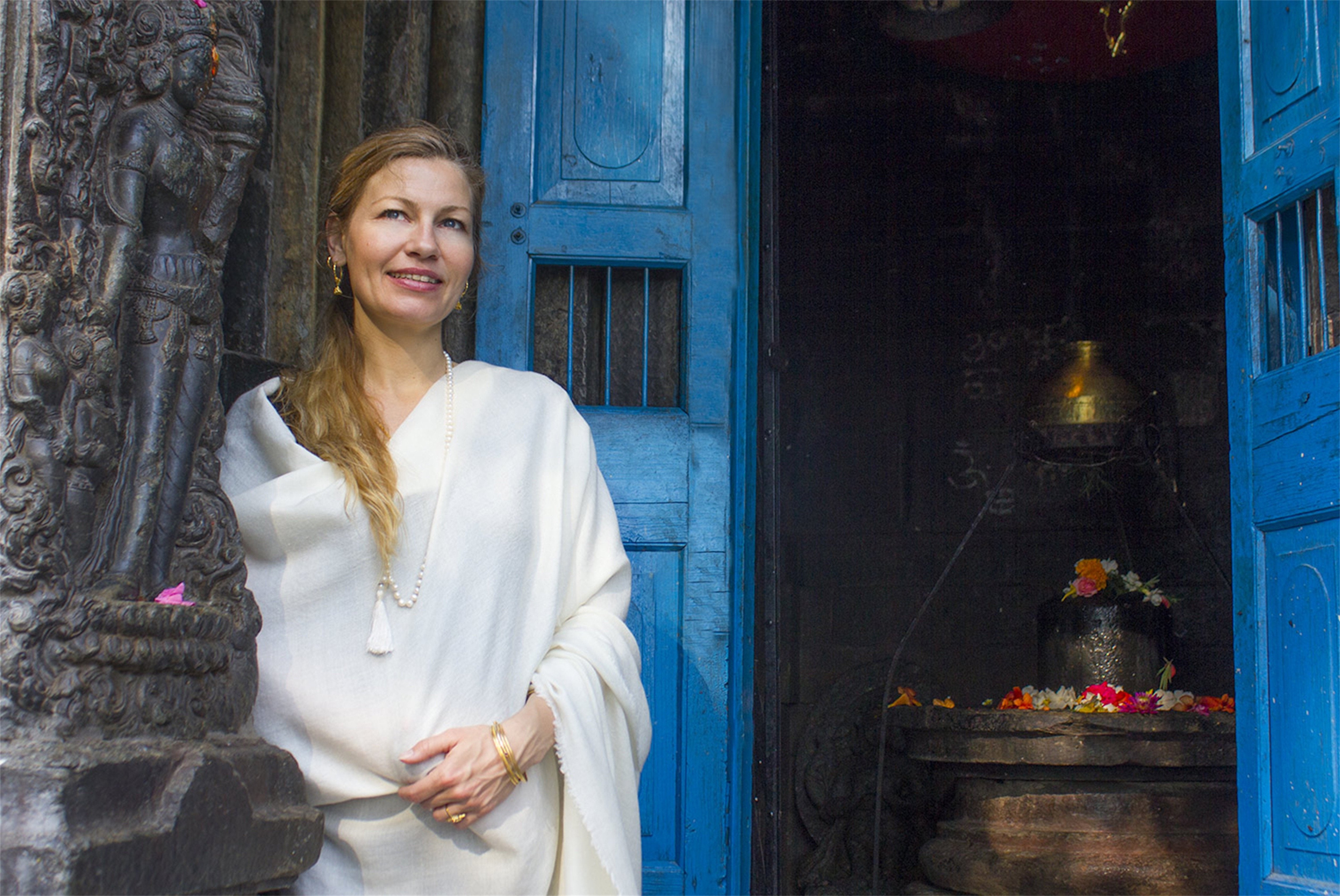 Woman in cream pashmina meditation shawl standing by a temple door, exuding calm and grace.