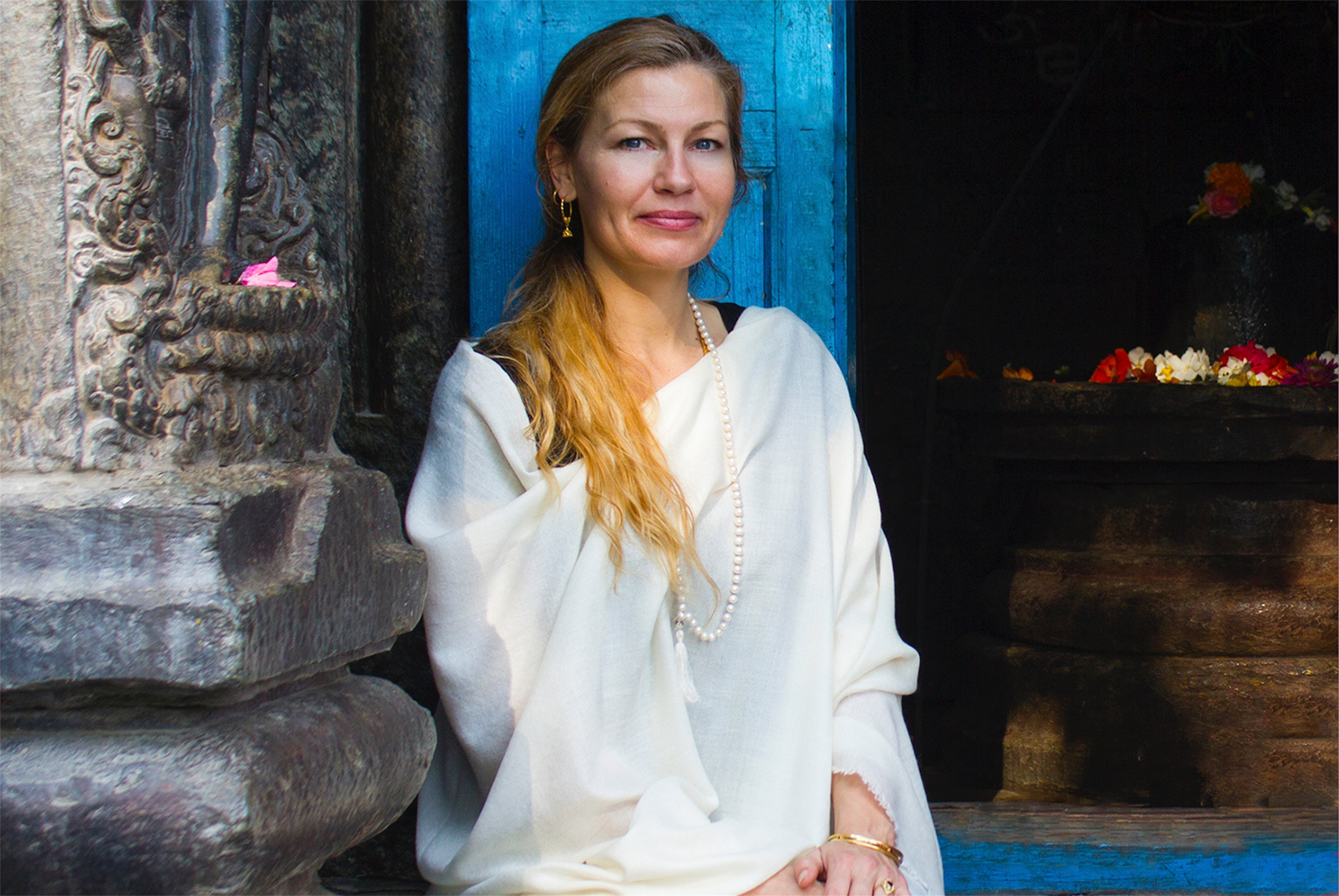 Woman in cream pashmina meditation shawl standing by a temple door, exuding calm and grace.