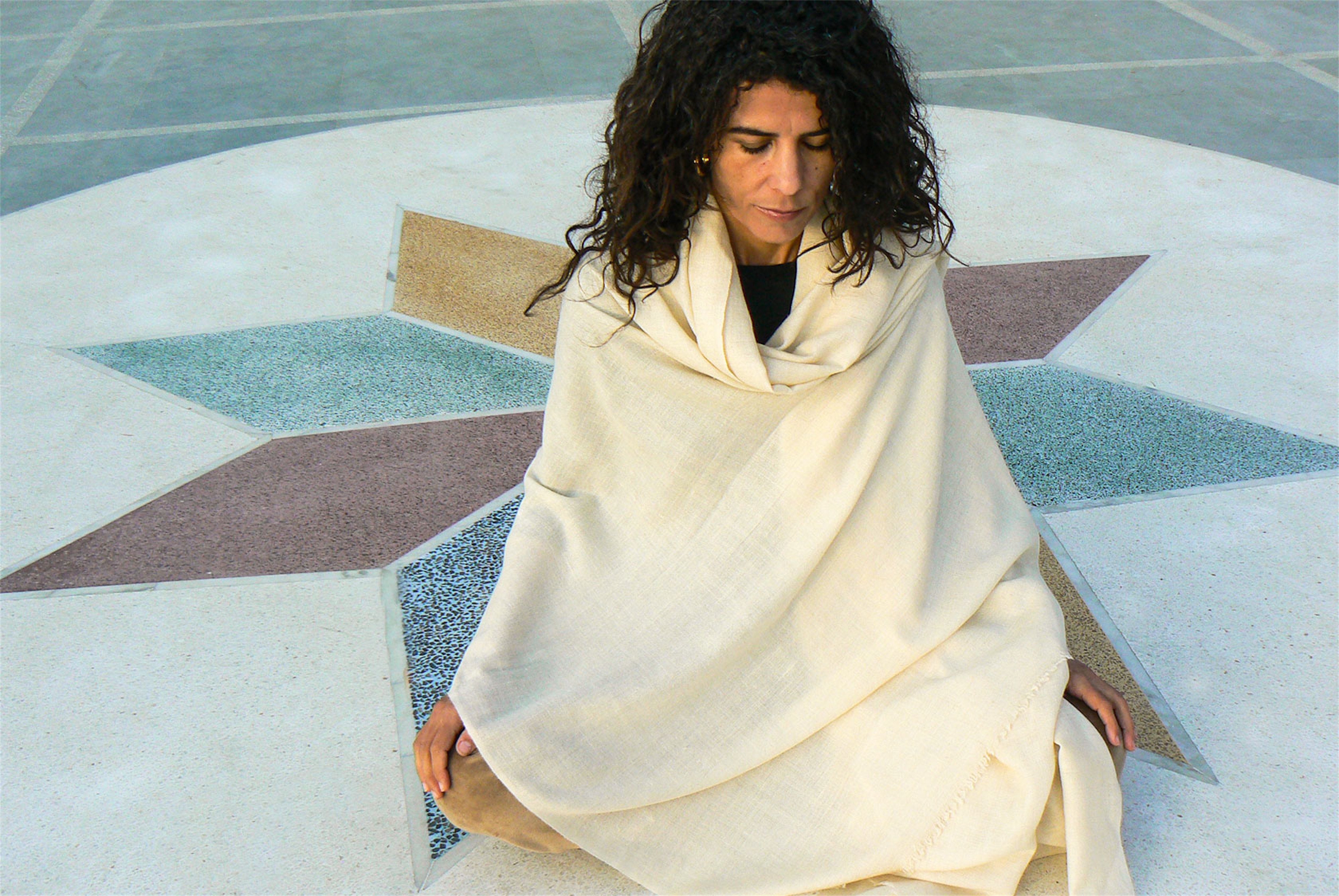 Meditating in a light cream shawl on a star-patterned ground, emphasizing the tranquil surroundings.