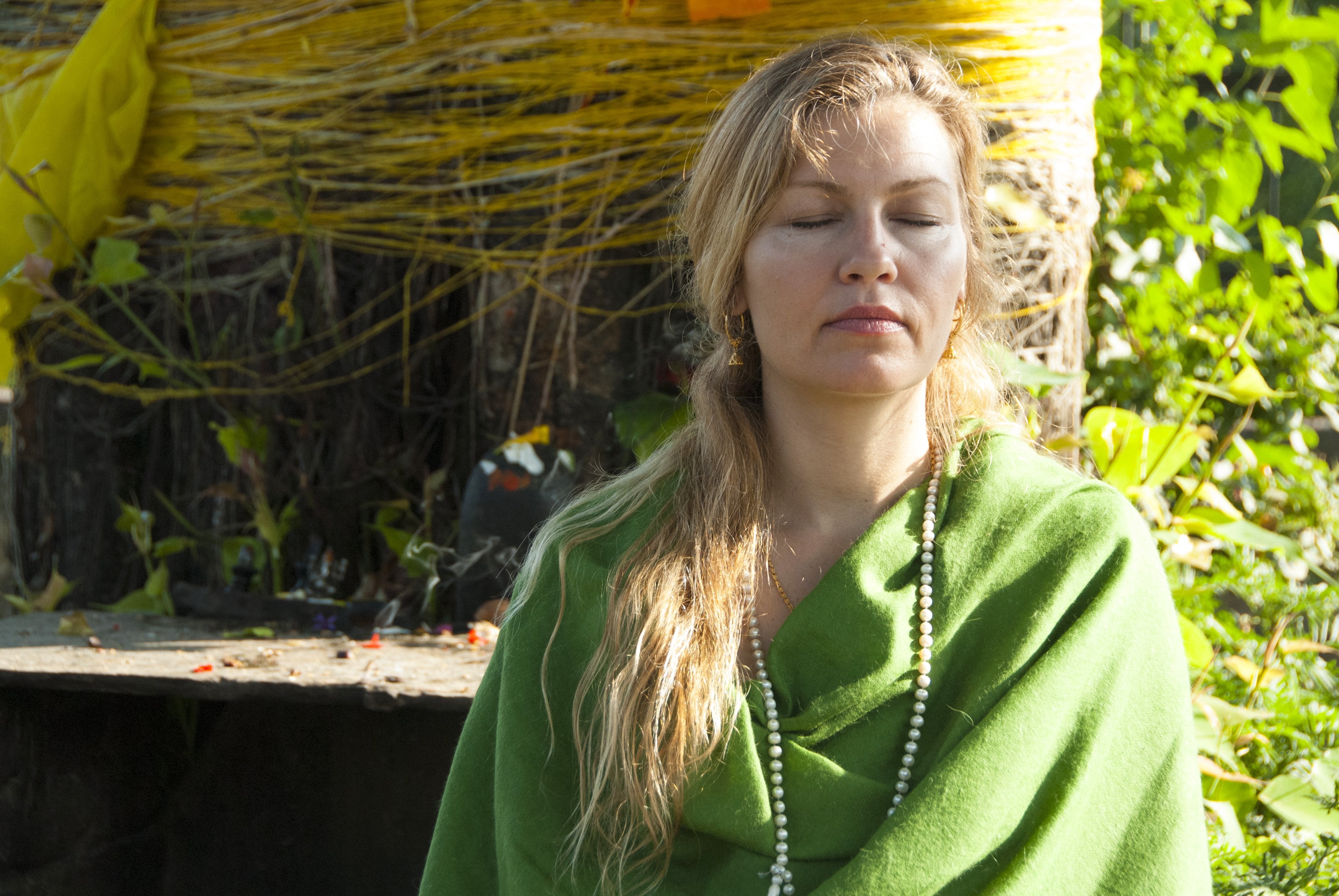 Woman in meditation wearing a green merino wool shawl, with a peaceful setting in the background.