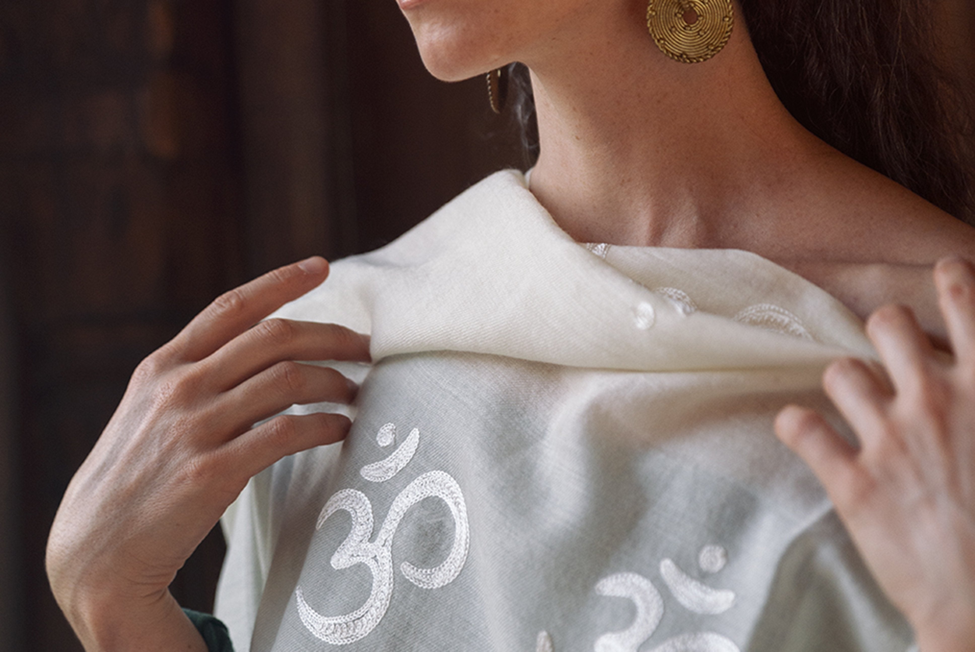 Close-up of woman’s hand holding a white shawl with Om embroidery.