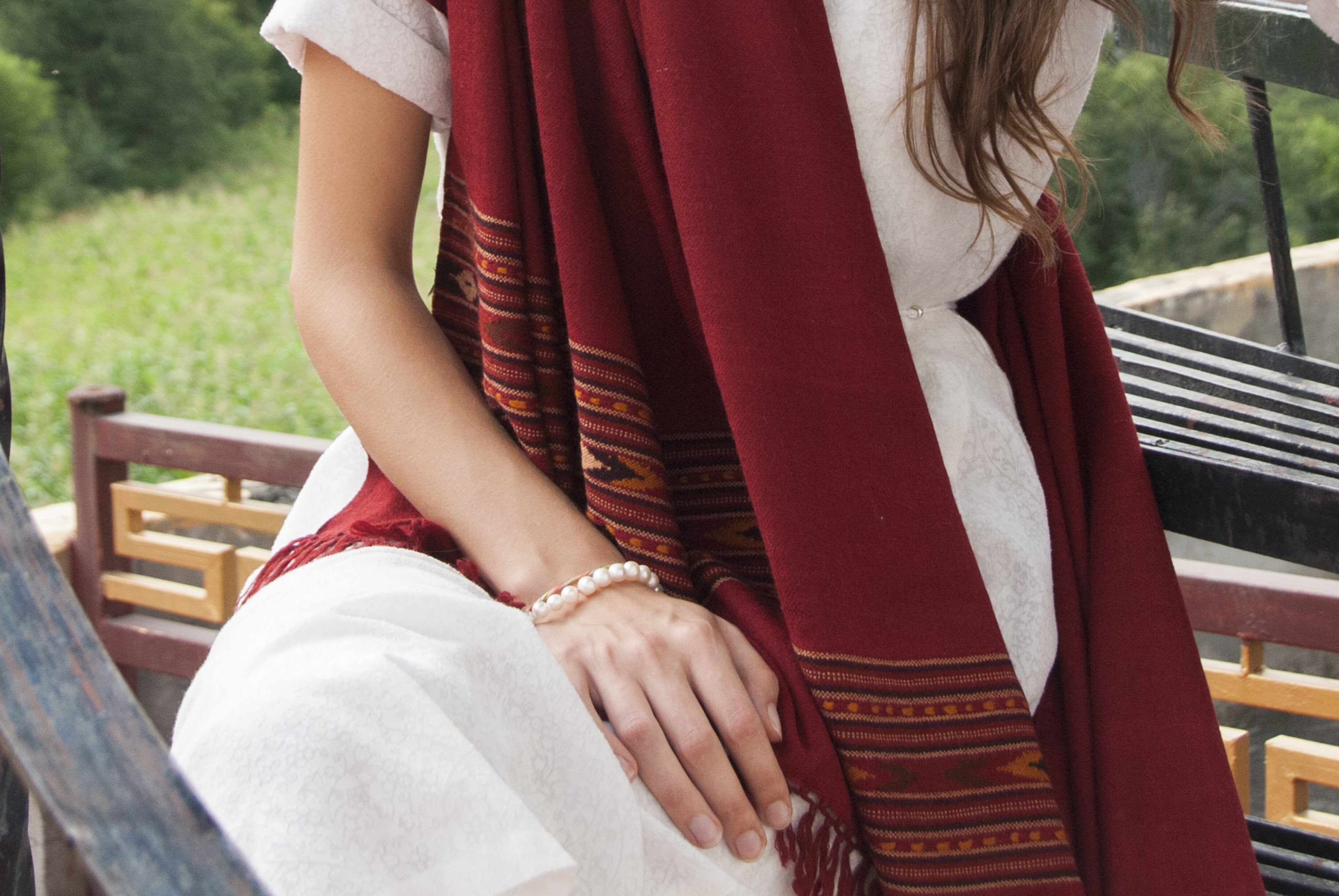 Woman wearing a burgundy red shawl, sitting on stone steps with a scenic mountain landscape in the background.