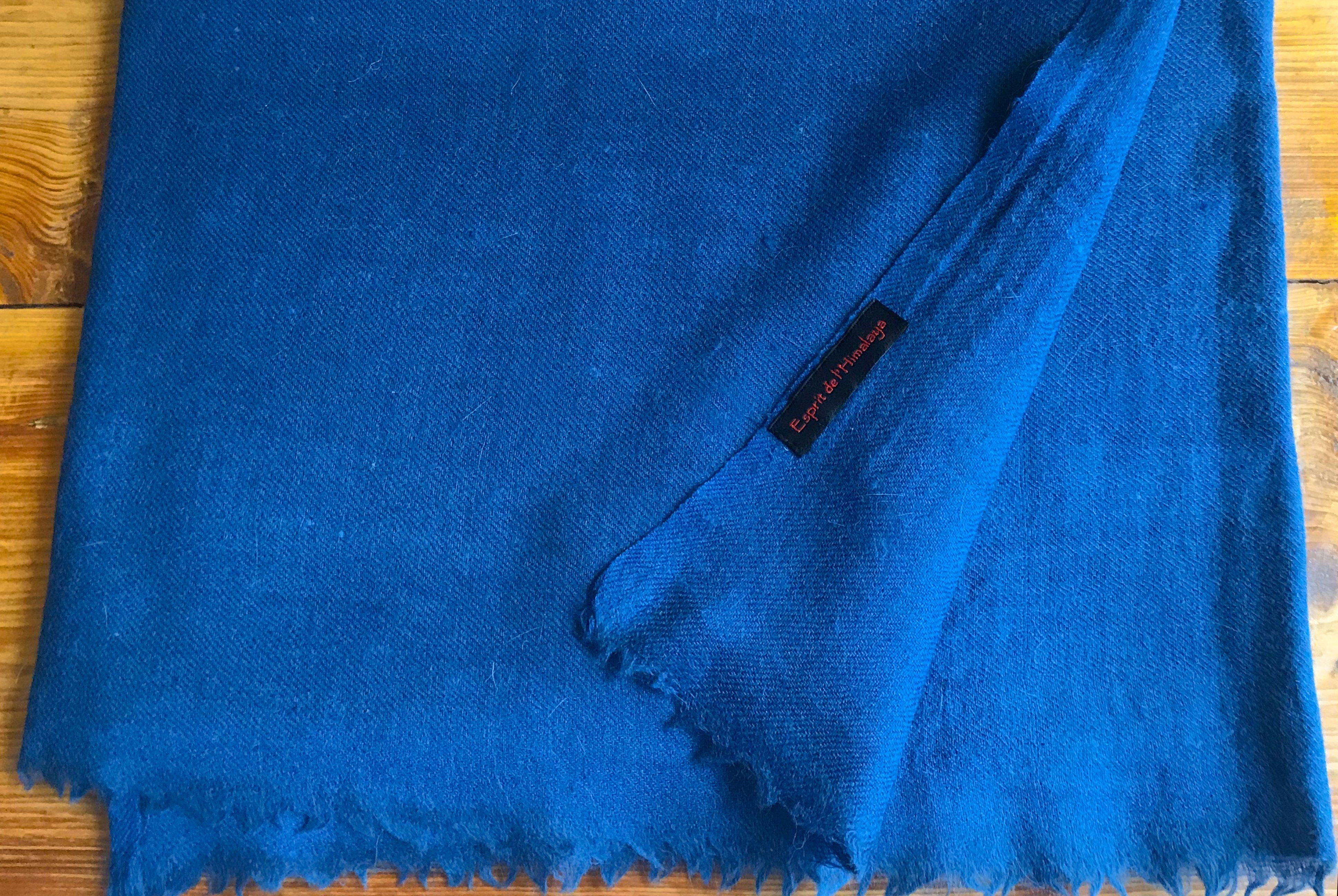 Medium blue merino wool and angora blend shawl folded neatly on a wooden surface.