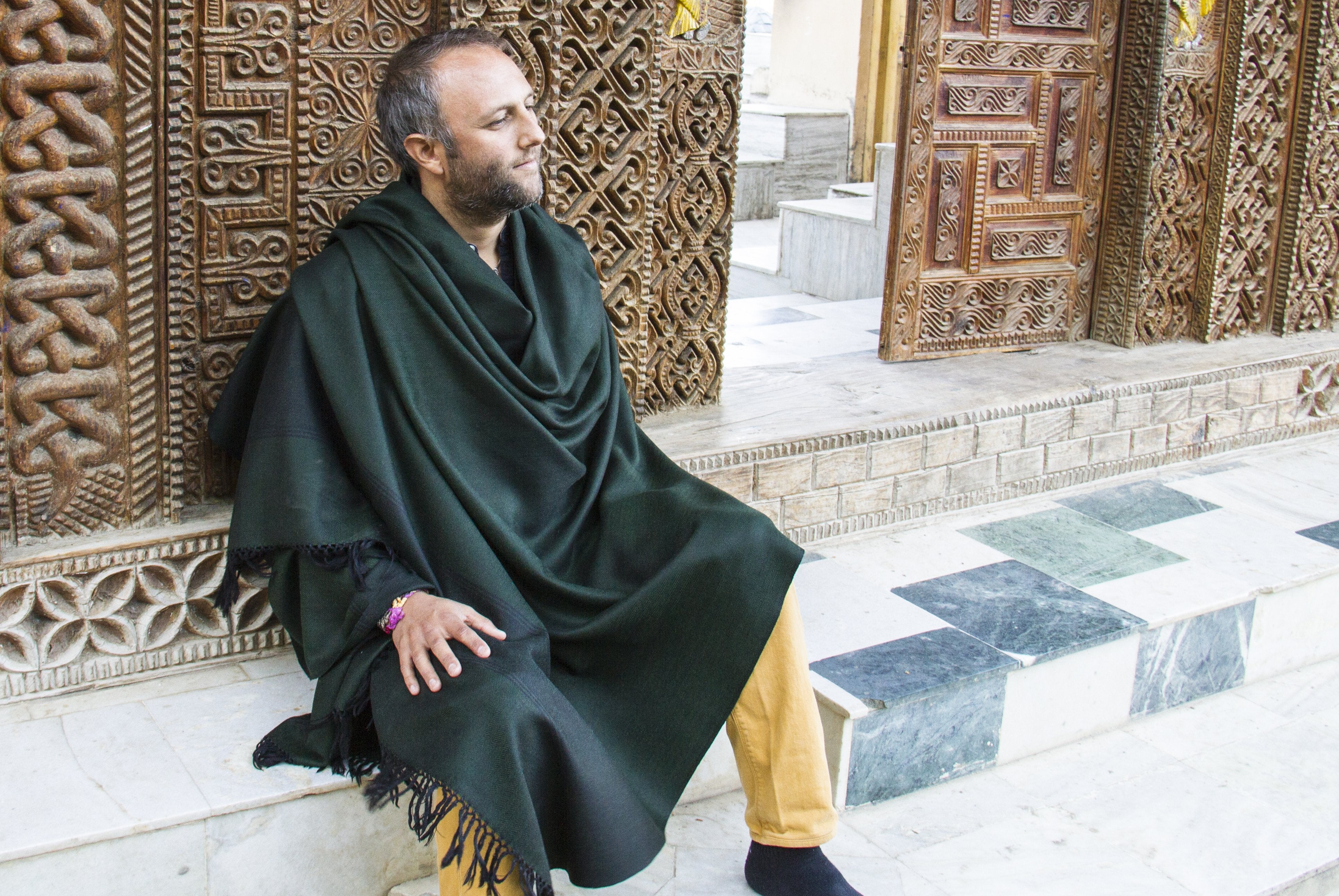 A serene man wearing a deep green Milarepa wool meditation shawl, seated against a beautifully carved wooden backdrop, exuding a tranquil vibe.