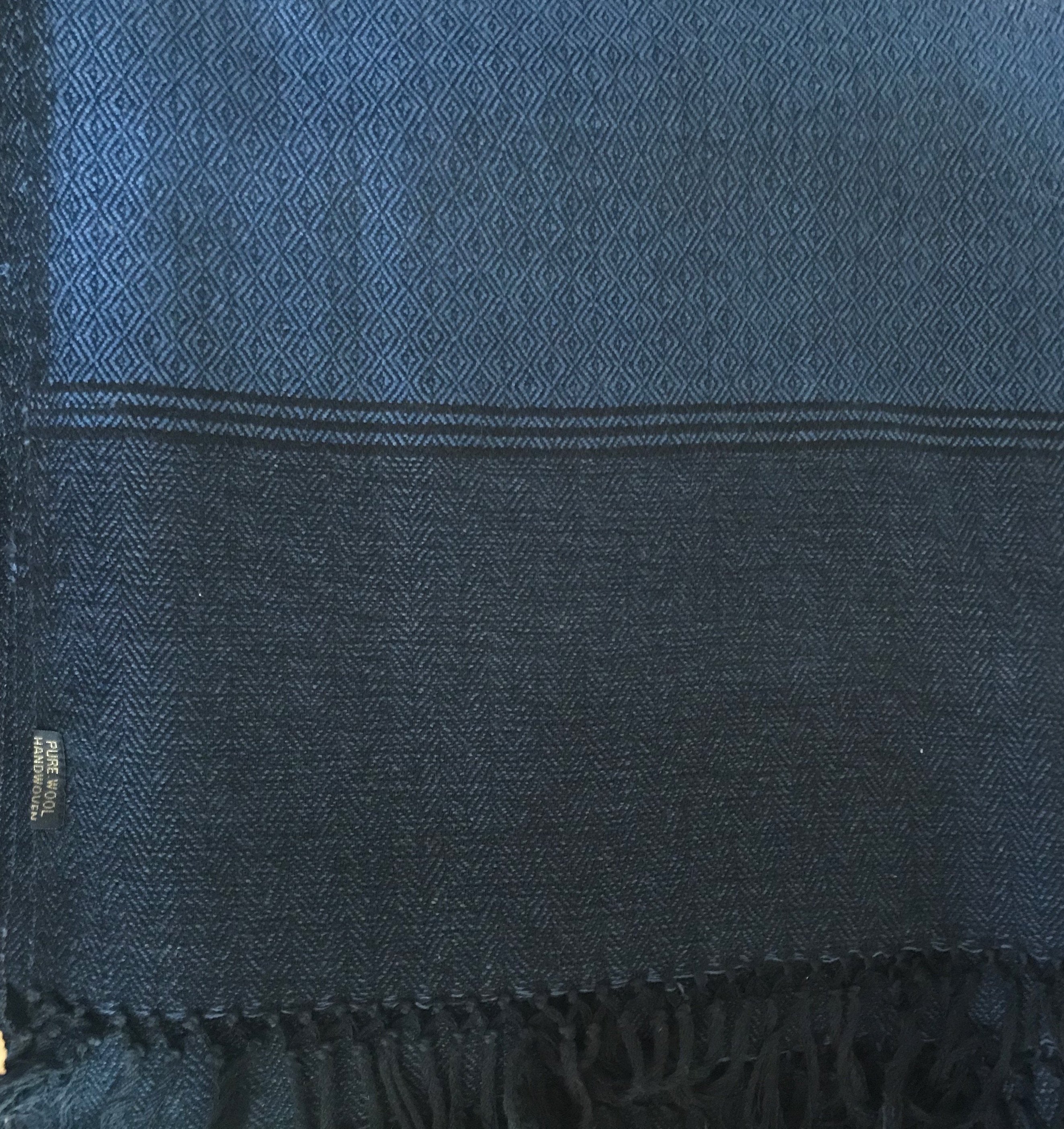 Close-up of a dark blue Milarepa large wool shawl featuring intricate diamond and herringbone patterns, with fringed edges.