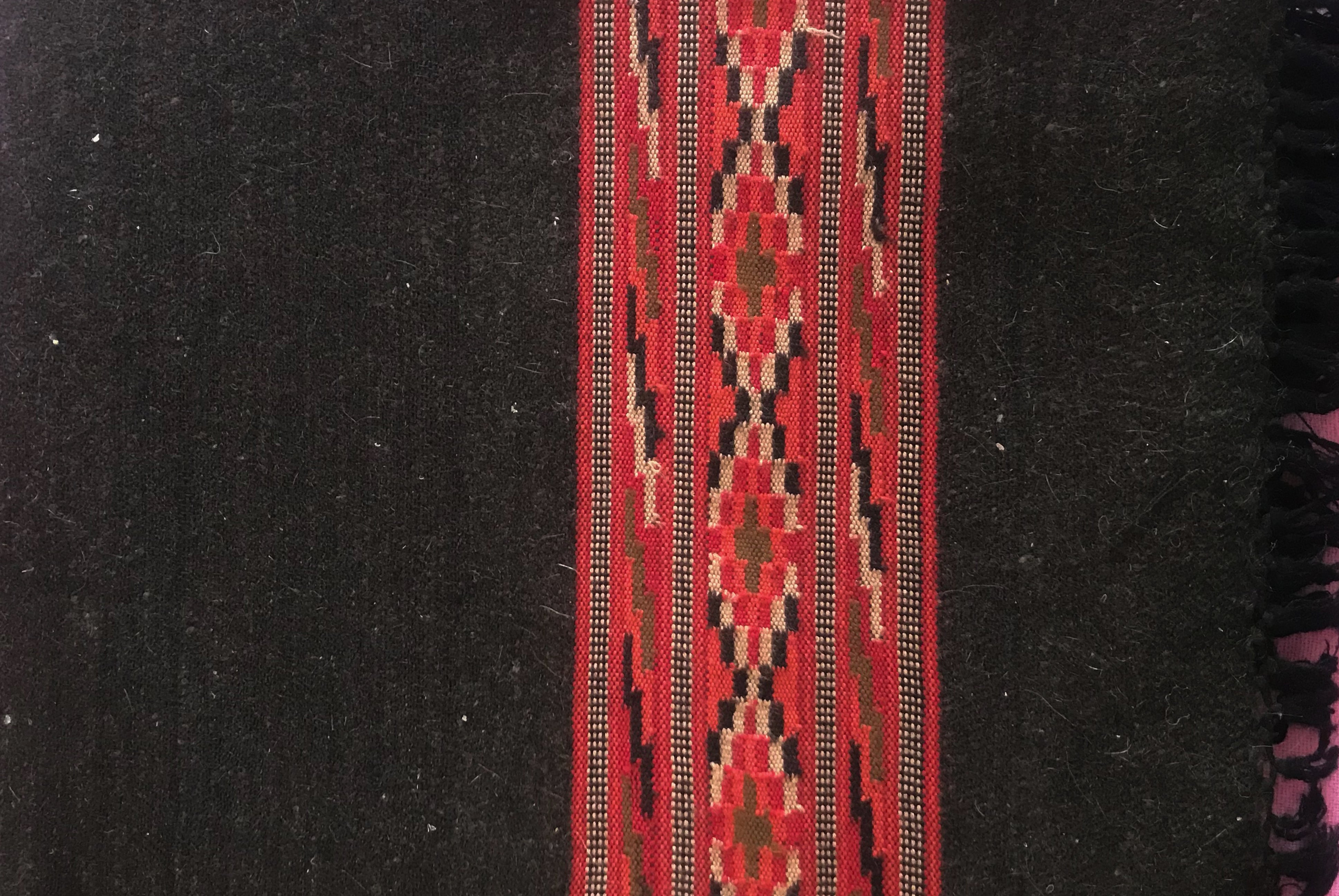 Close-up of a pure yak wool meditation blanket in black with a traditional red and brown patterned border.