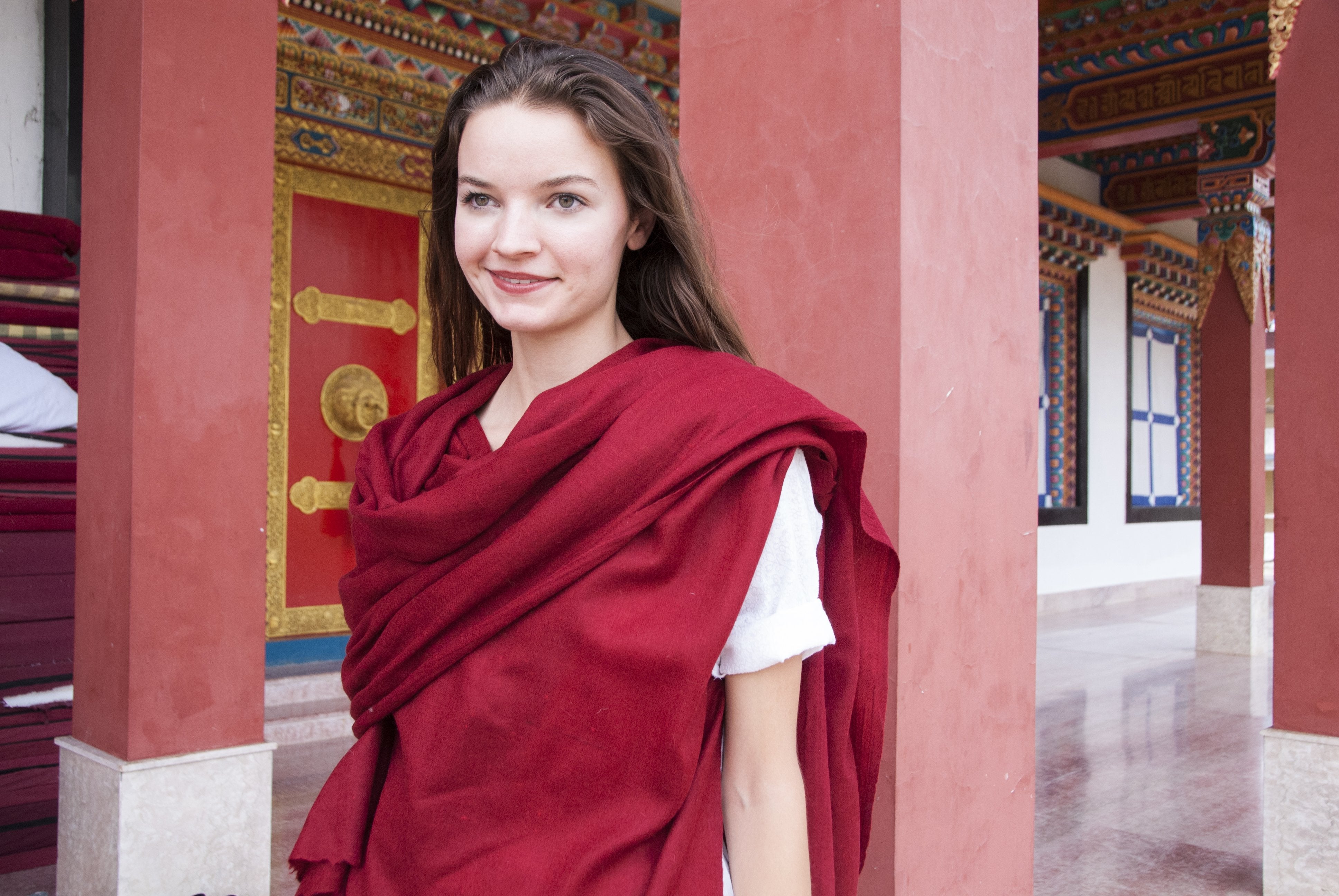 This image showcases a beautifully crafted red angora shawl elegantly draped over the shoulders of a model, set against a traditional architectural backdrop.