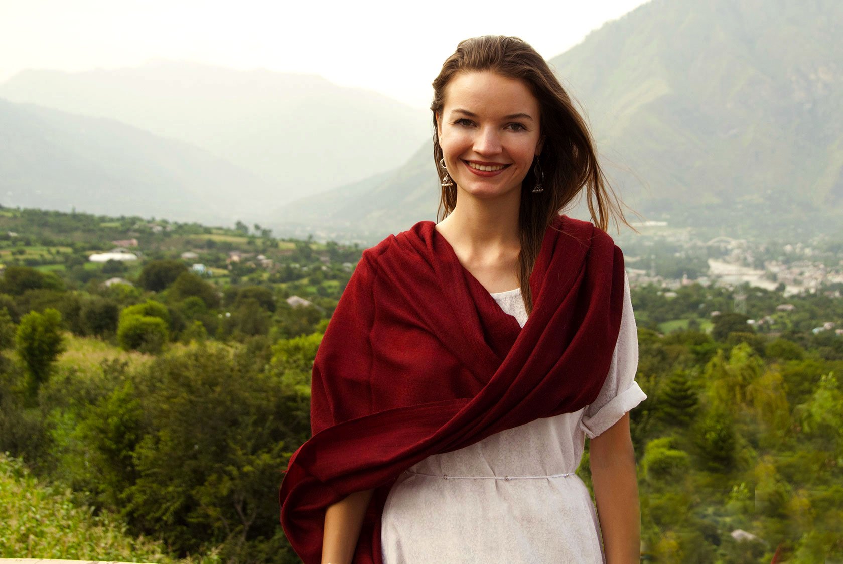 A woman wearing a red wool meditation shawl around her shoulders, smiling in a natural setting.