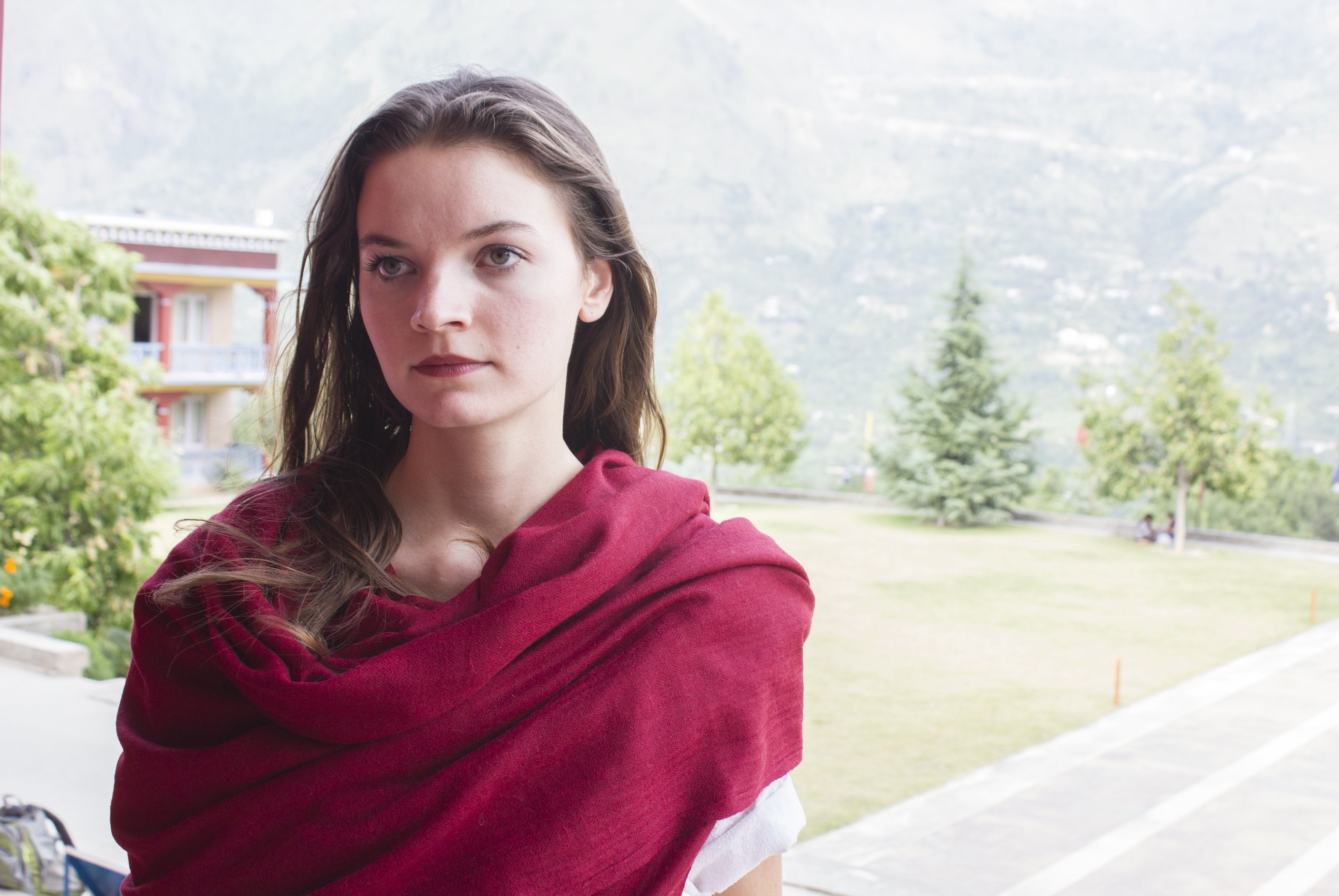 A woman wearing a red wool meditation shawl around her shoulders in a natural setting.