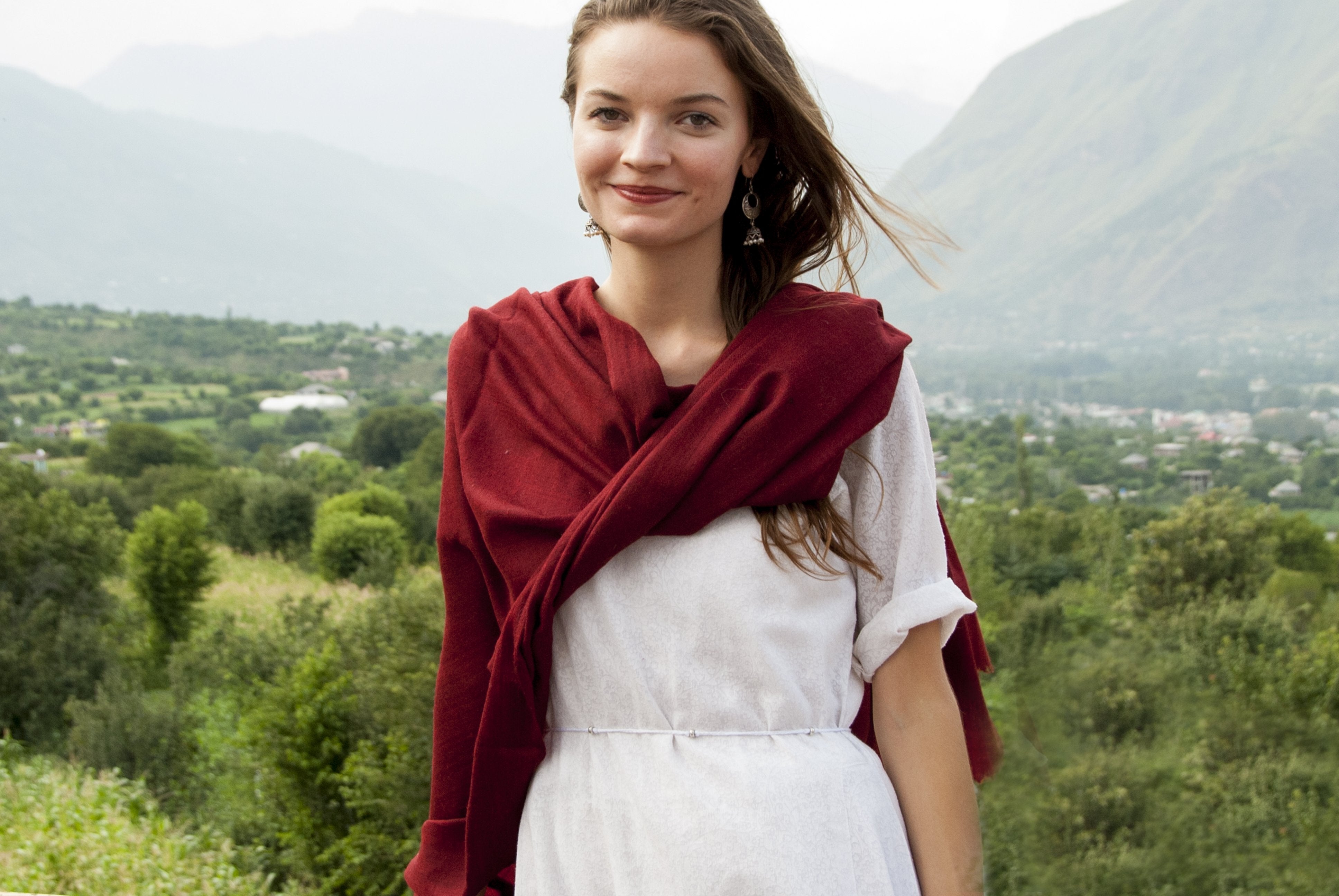 A woman wearing a red wool meditation shawl around her shoulders, smiling in a natural setting.