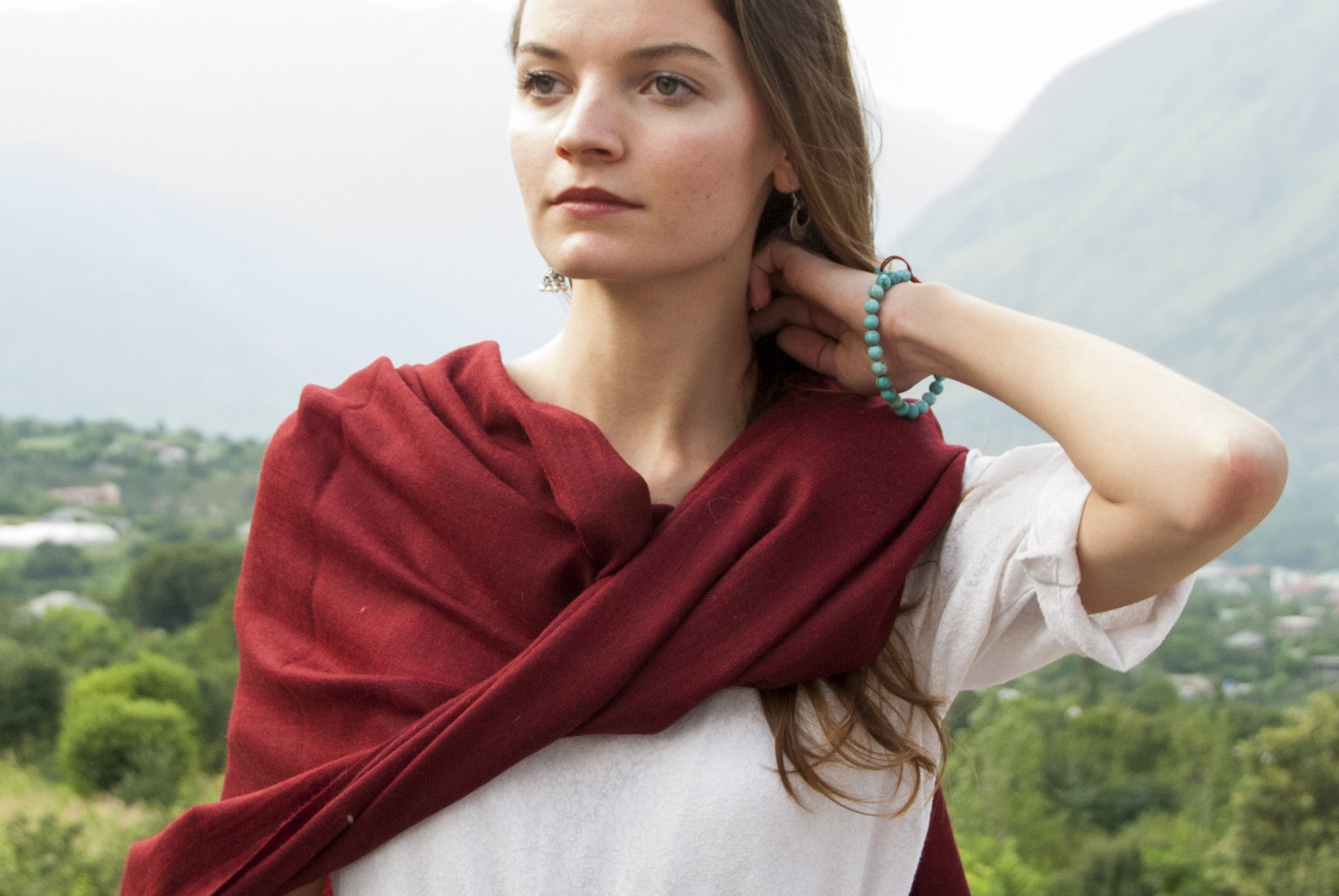 A woman wearing a red wool meditation shawl around her shoulders in a natural setting.